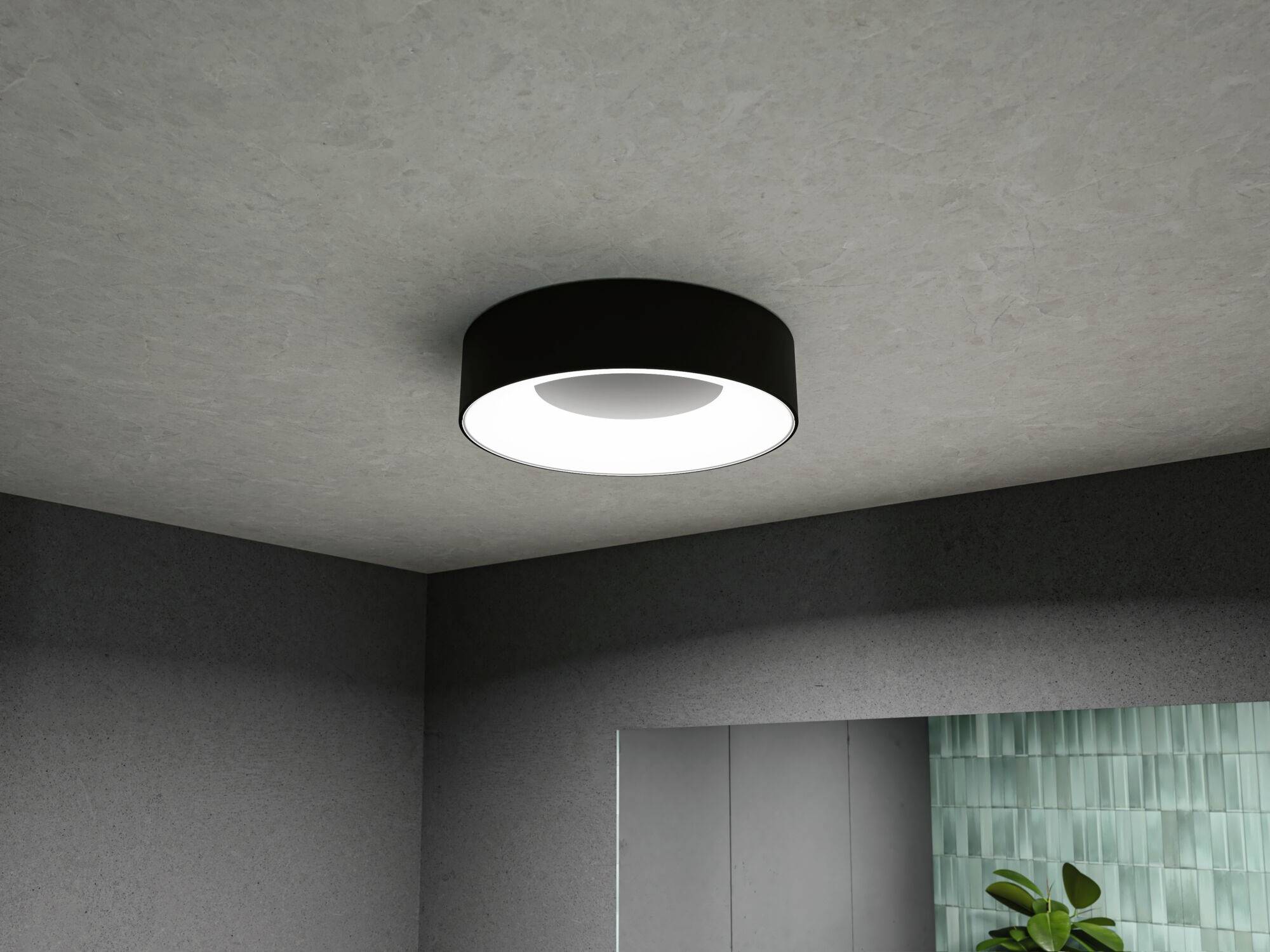 Eine runde, moderne Deckenleuchte leuchtet einen Raum aus. Wände sind grau, ein Pflanze ist in der Ecke sichtbar.