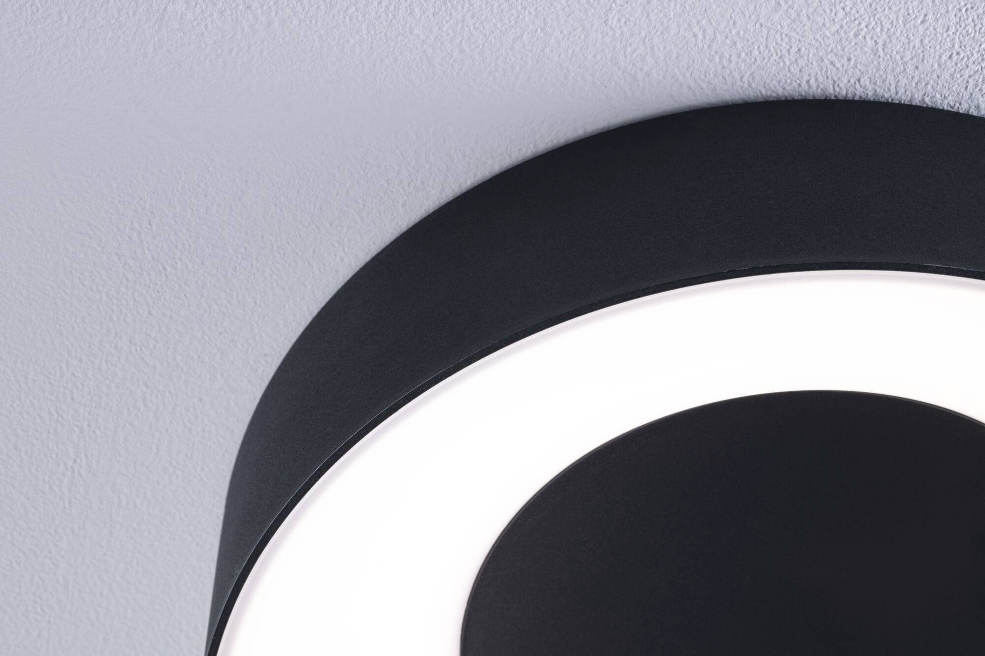Eine schwarze, runde Deckenleuchte mit einem leuchtenden, weißen Rand an einer grauen Decke.