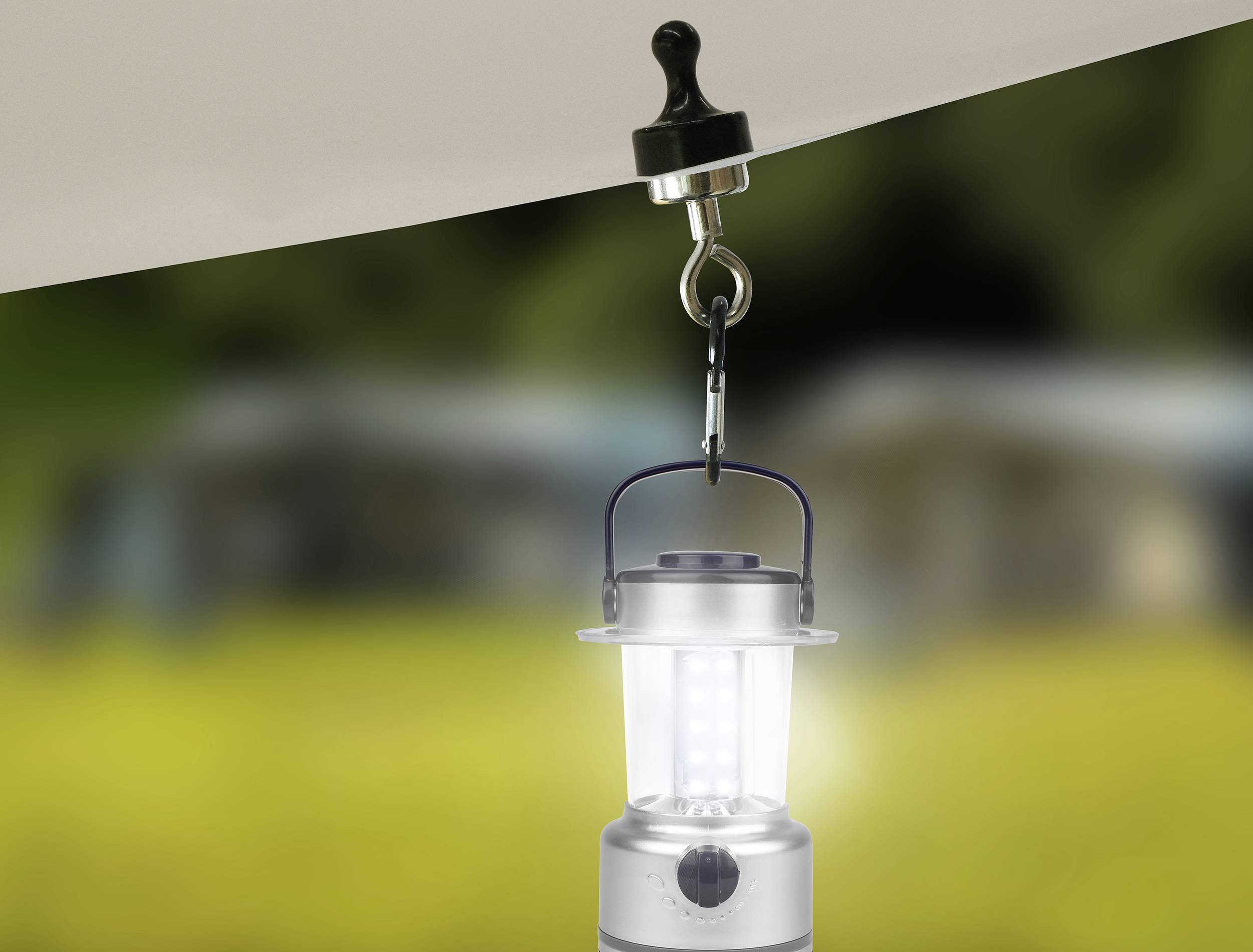 Campinglaterne hängt an einem Haken unter einer Zeltplane vor einem verschwommenen Hintergrund im Freien.
