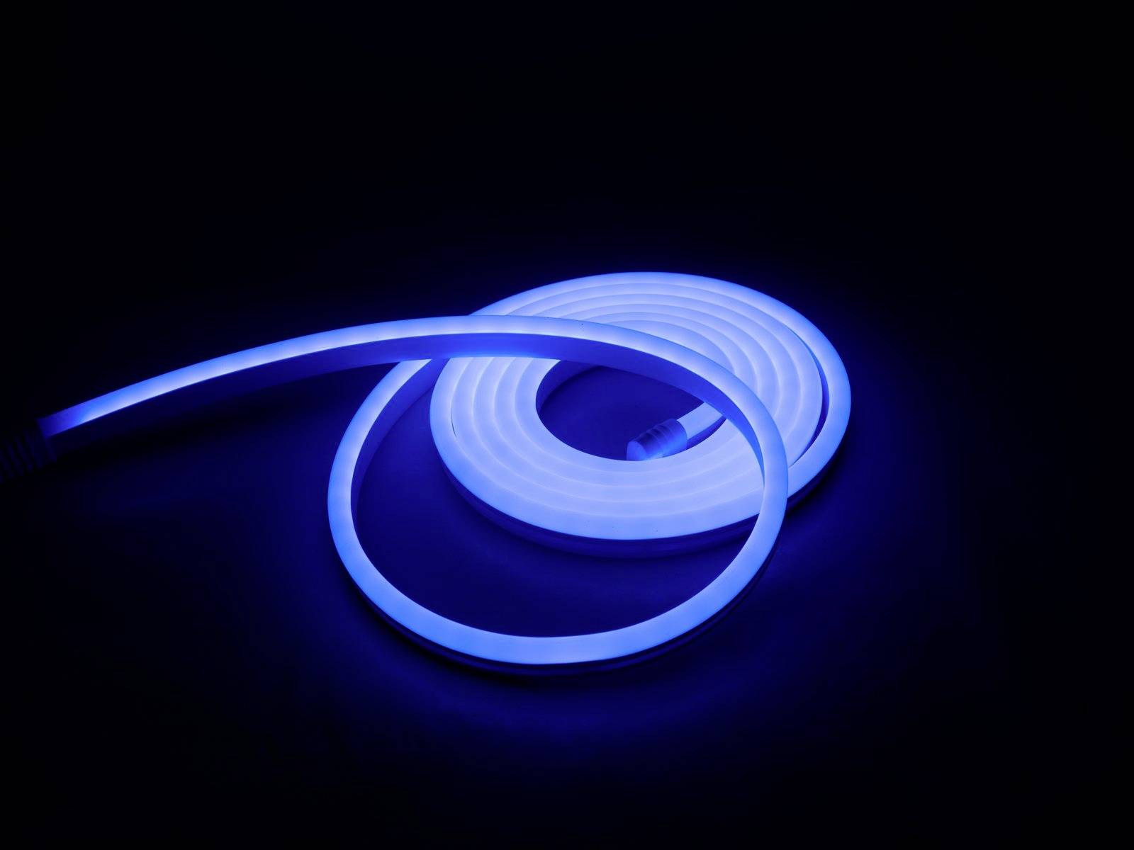 Ein blaues LED-Lichtband liegt aufgerollt auf einer dunklen Oberfläche und leuchtet hell.