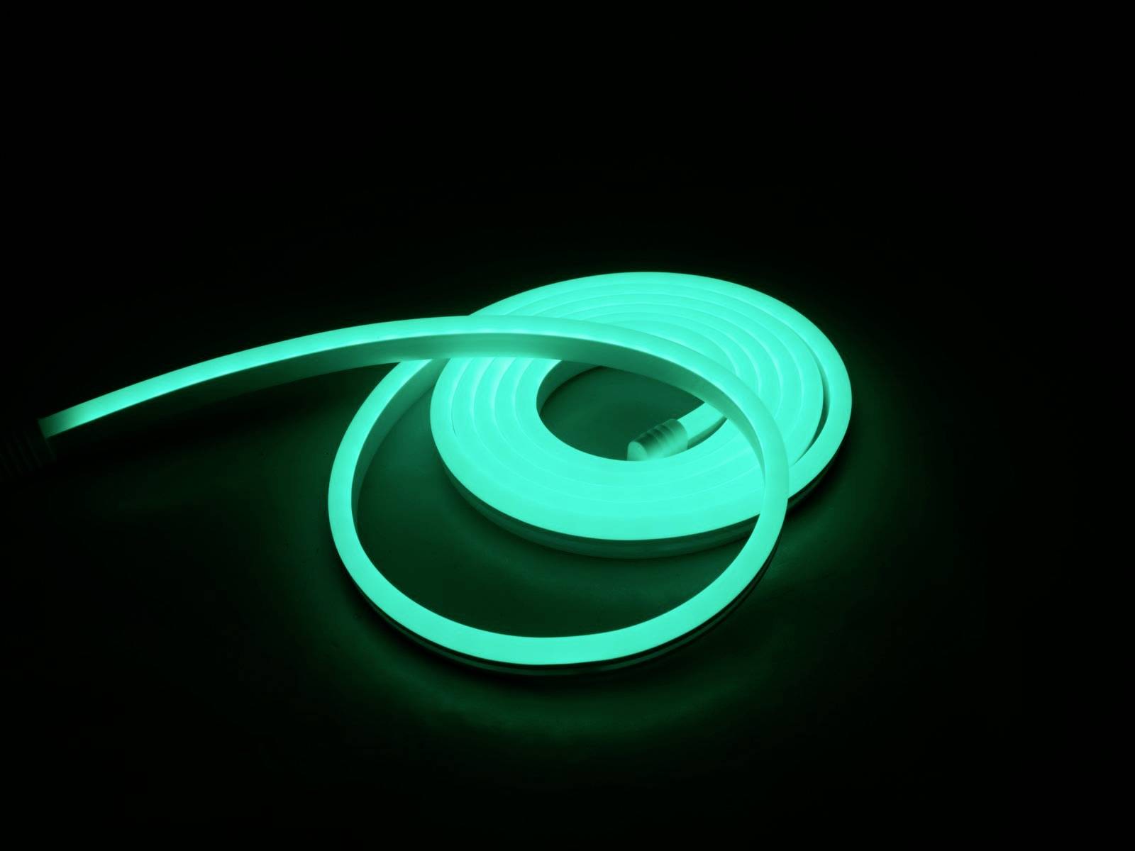 Ein leuchtender, grüner LED-Streifen liegt in einer Spirale auf schwarzem Hintergrund und strahlt helles Licht aus.