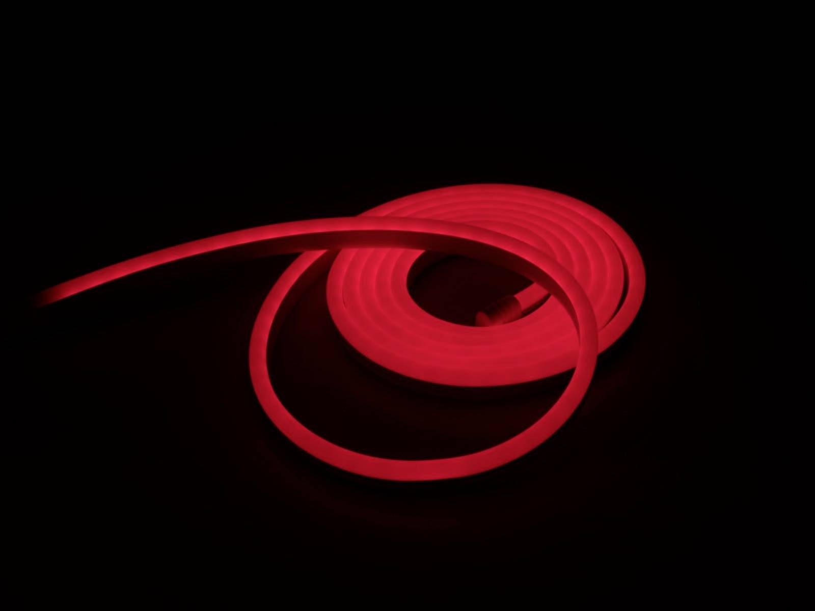 Ein leuchtender roter LED-Streifen, der aufgerollt auf einem dunklen Hintergrund liegt, sorgt für einen markanten Lichteffekt.