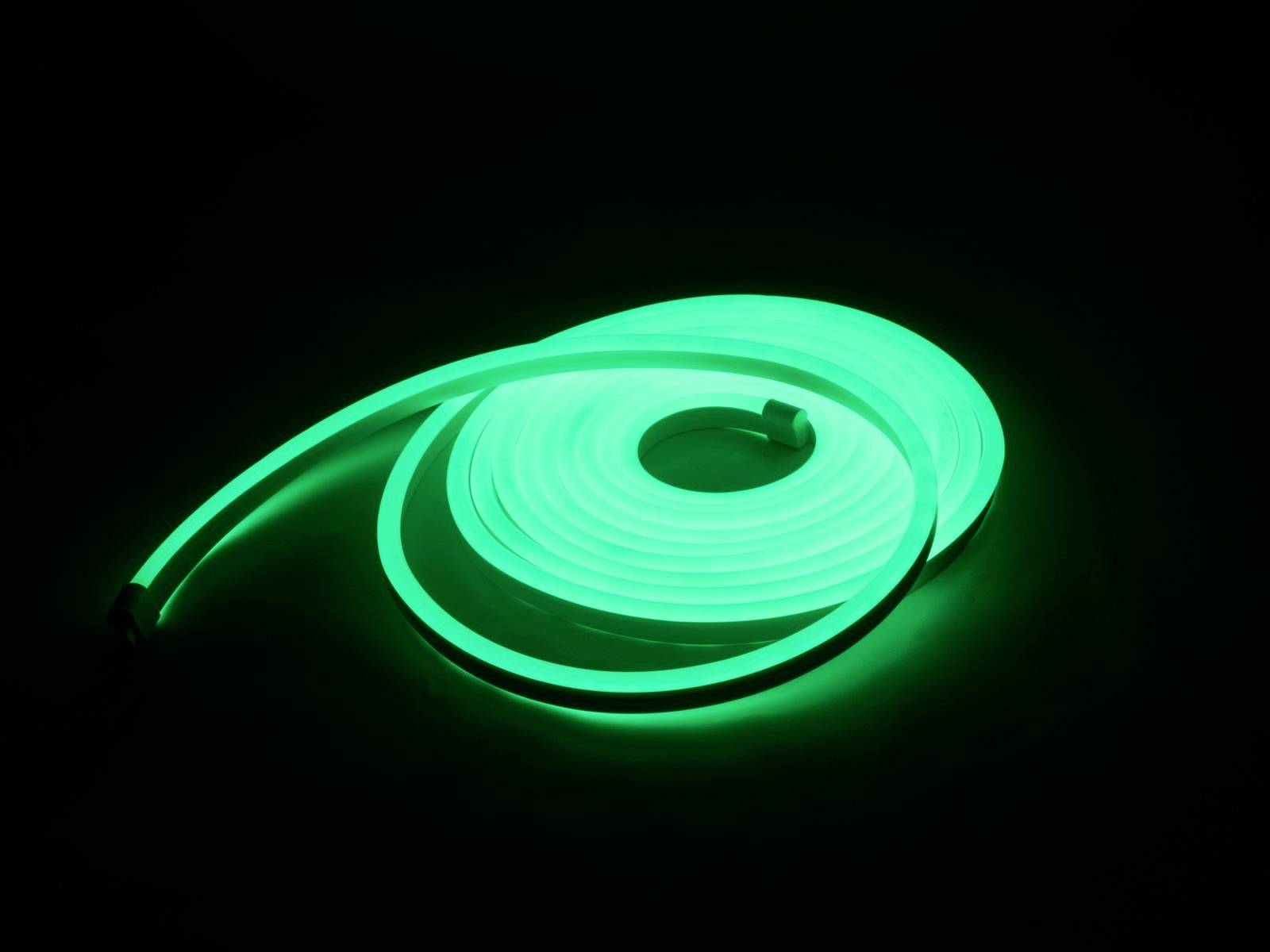 Ein grünes LED-Lichtband leuchtet intensiv in der Dunkelheit, aufgerollt auf einer glatten Oberfläche.