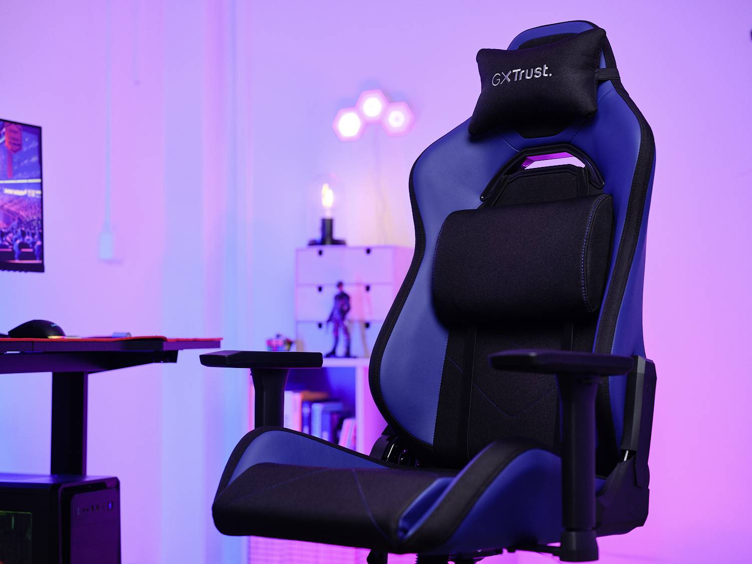 Blauer Gaming-Stuhl mit Kopf- und Lendenkissen vor einem Schreibtisch in einem Raum mit violett-blauer Beleuchtung.