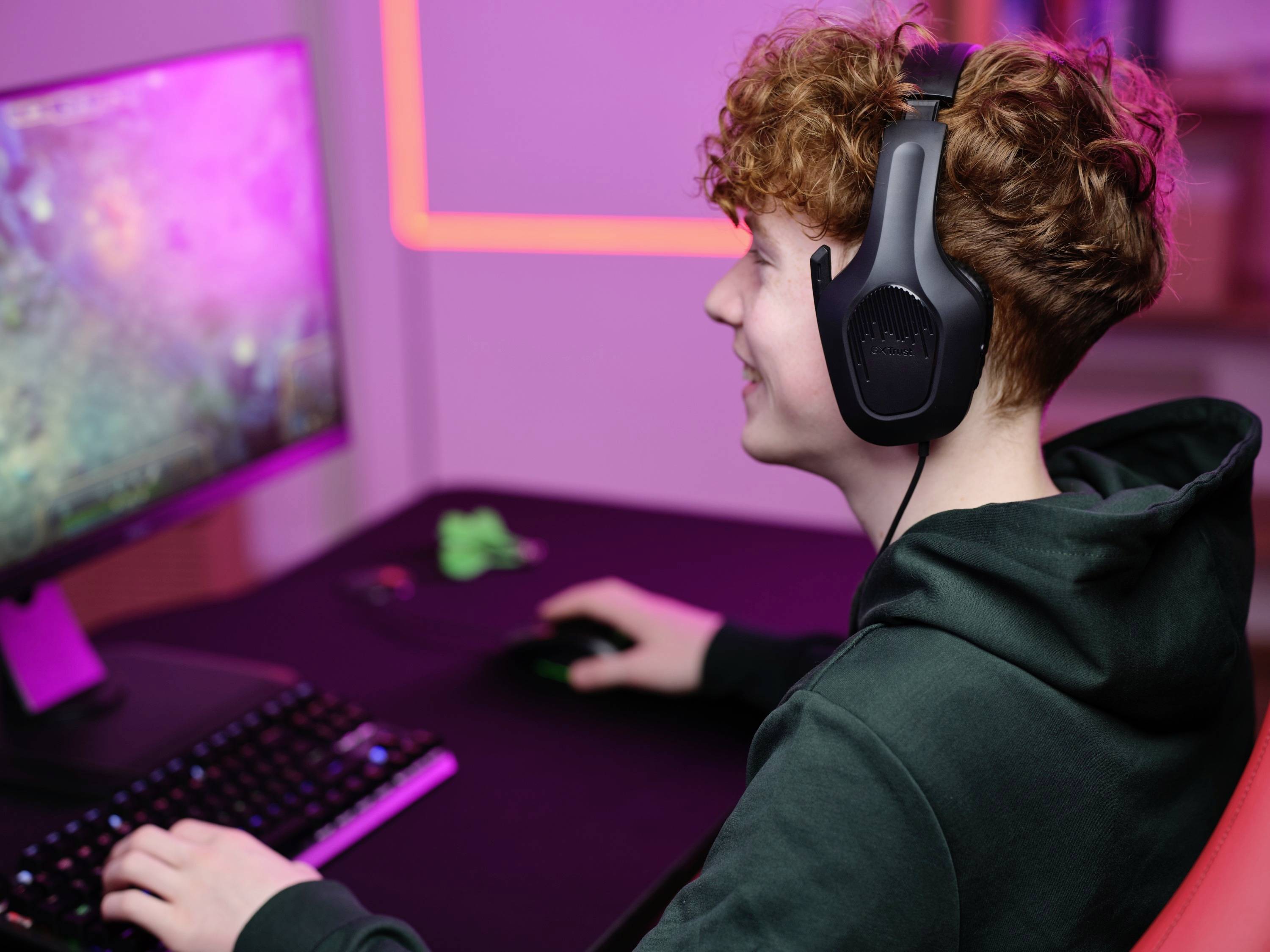 Eine Person mit Kopfhörern spielt an einem Computer, der von pinkem Licht beleuchtet wird.