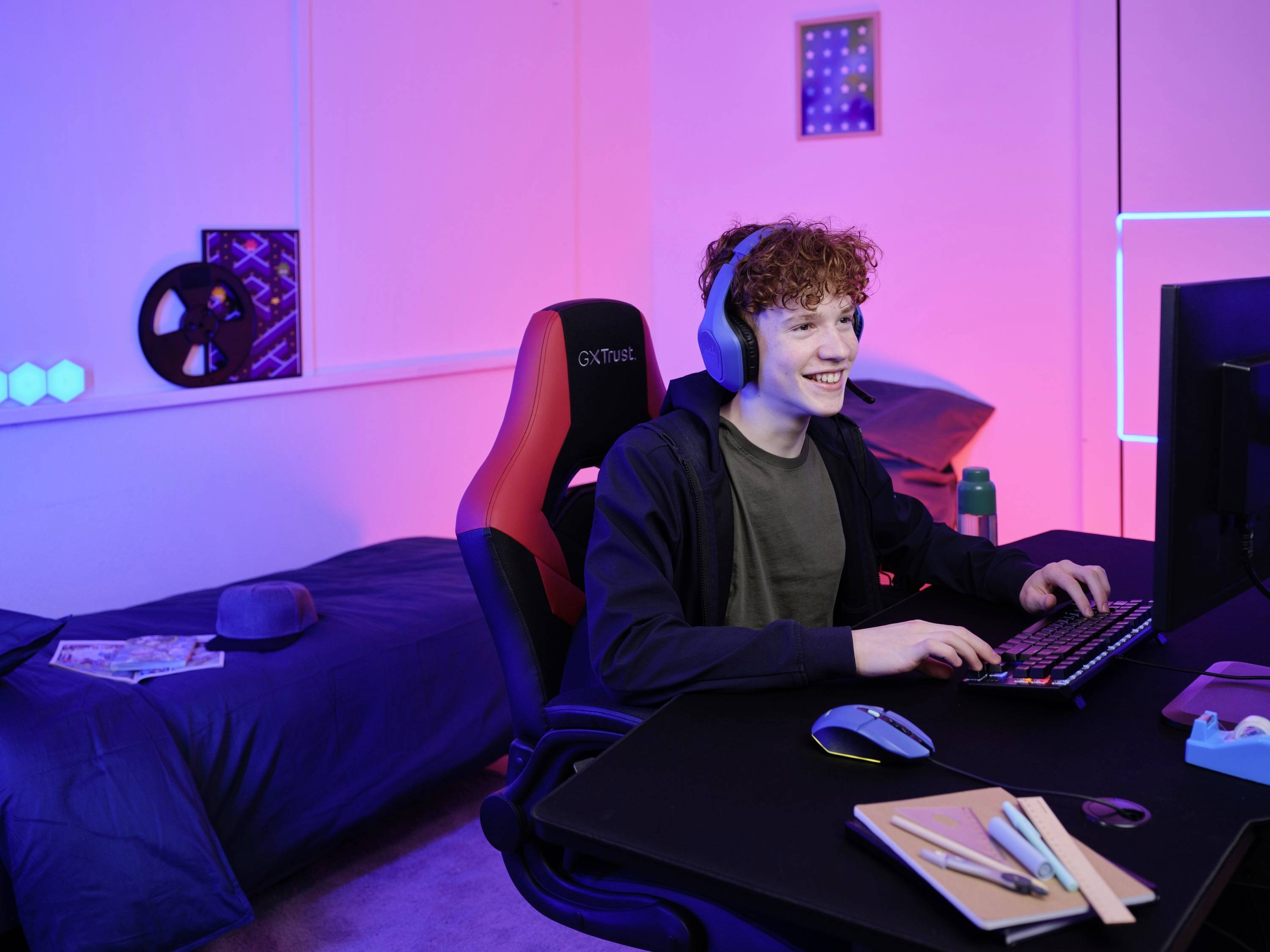 Ein junger Mann mit Kopfhörern sitzt freudig an einem Schreibtisch vor einem Computer in einem modern eingerichteten Zimmer.