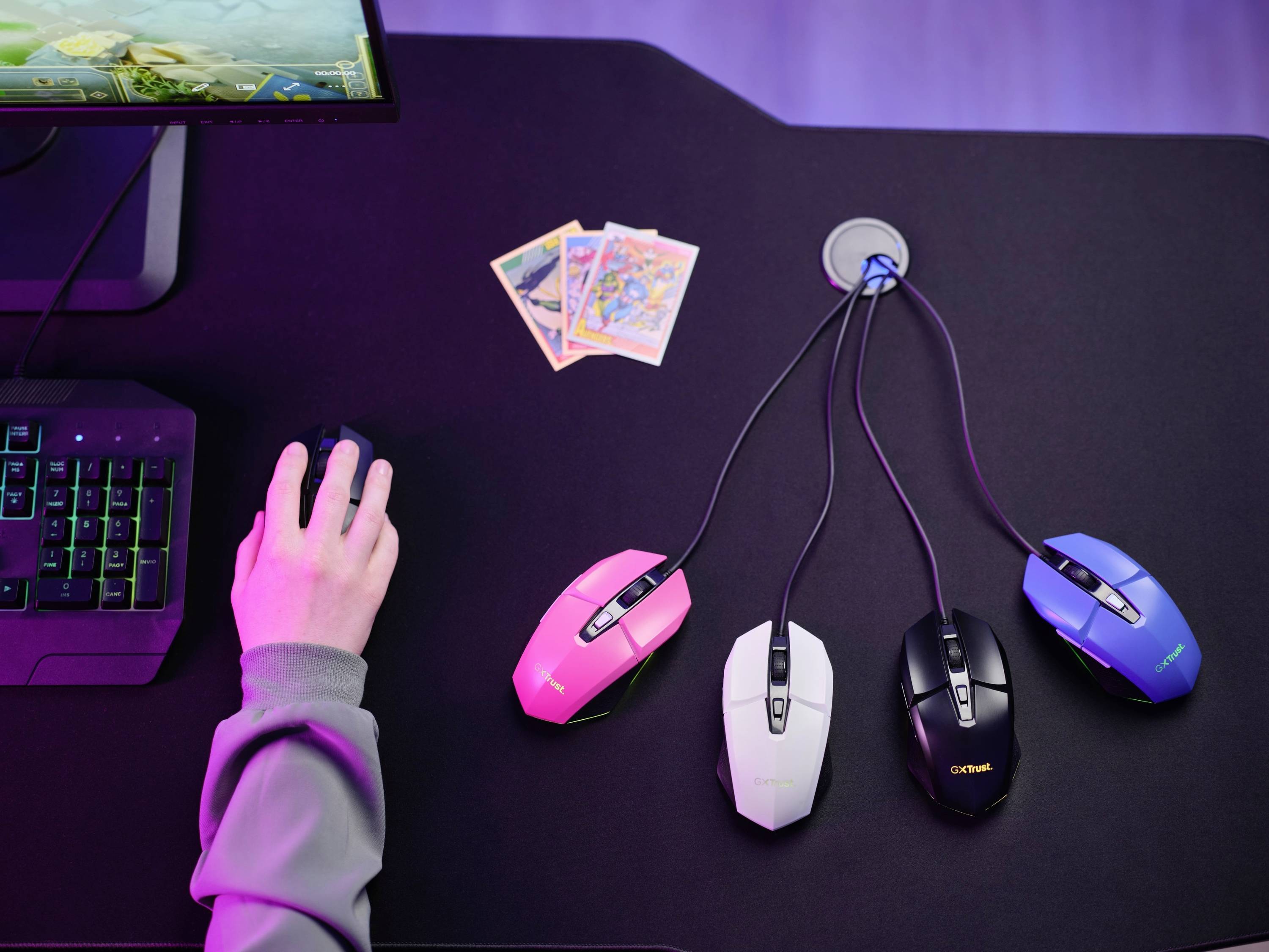 Eine Hand bedient eine Computermaus auf einem Tisch mit drei weiteren Mäusen und Spielkarten. Ein Monitor zeigt ein Spiel an.