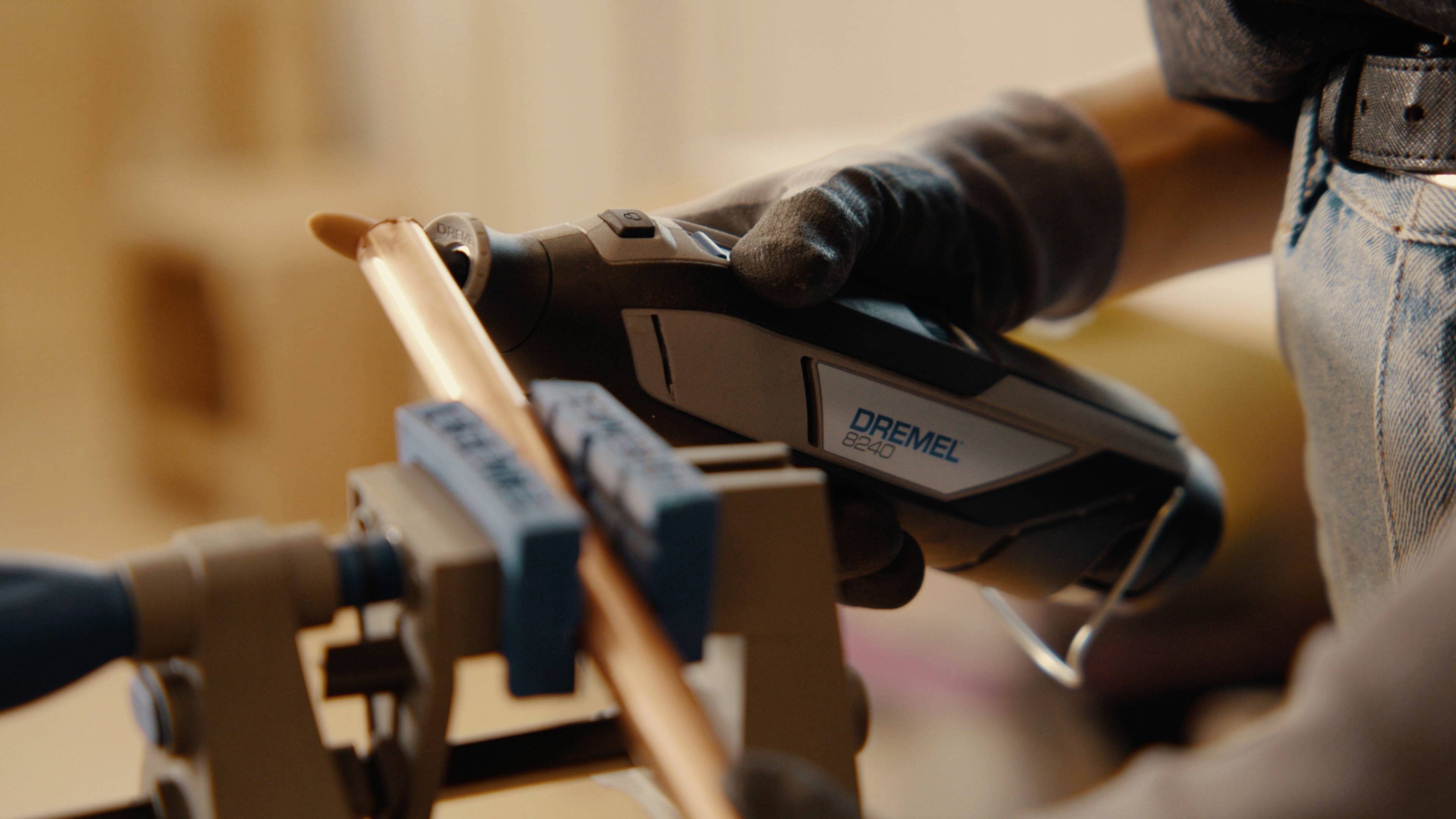 Eine Person bearbeitet mit einem Dremel-Werkzeug ein Kupferrohr, das in einem Schraubstock eingespannt ist. Sie trägt einen Handschuh.