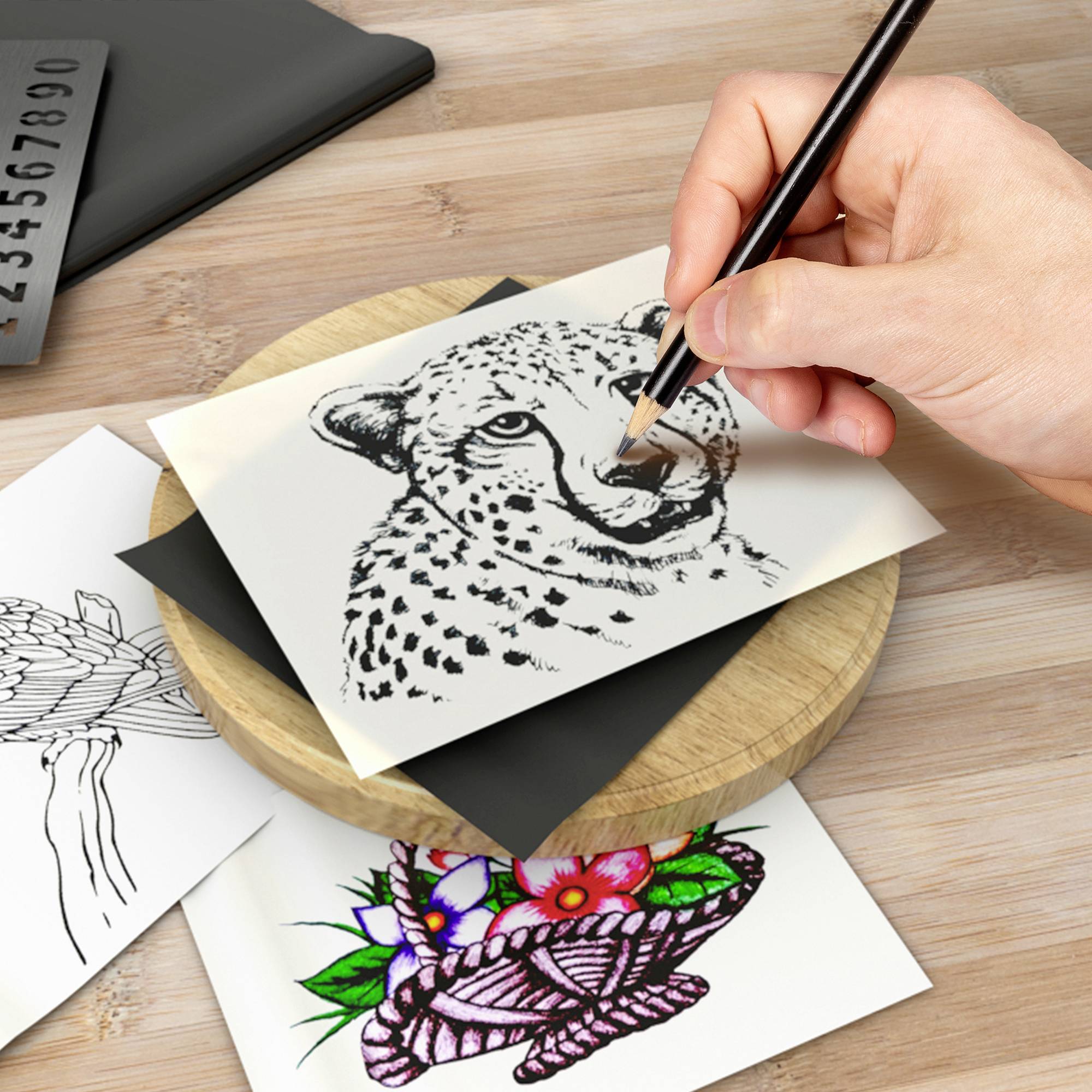 Eine Hand zeichnet einen Gepardenkopf auf ein Blatt Papier. Daneben liegen weitere Illustrationen, darunter Blumenmotive.