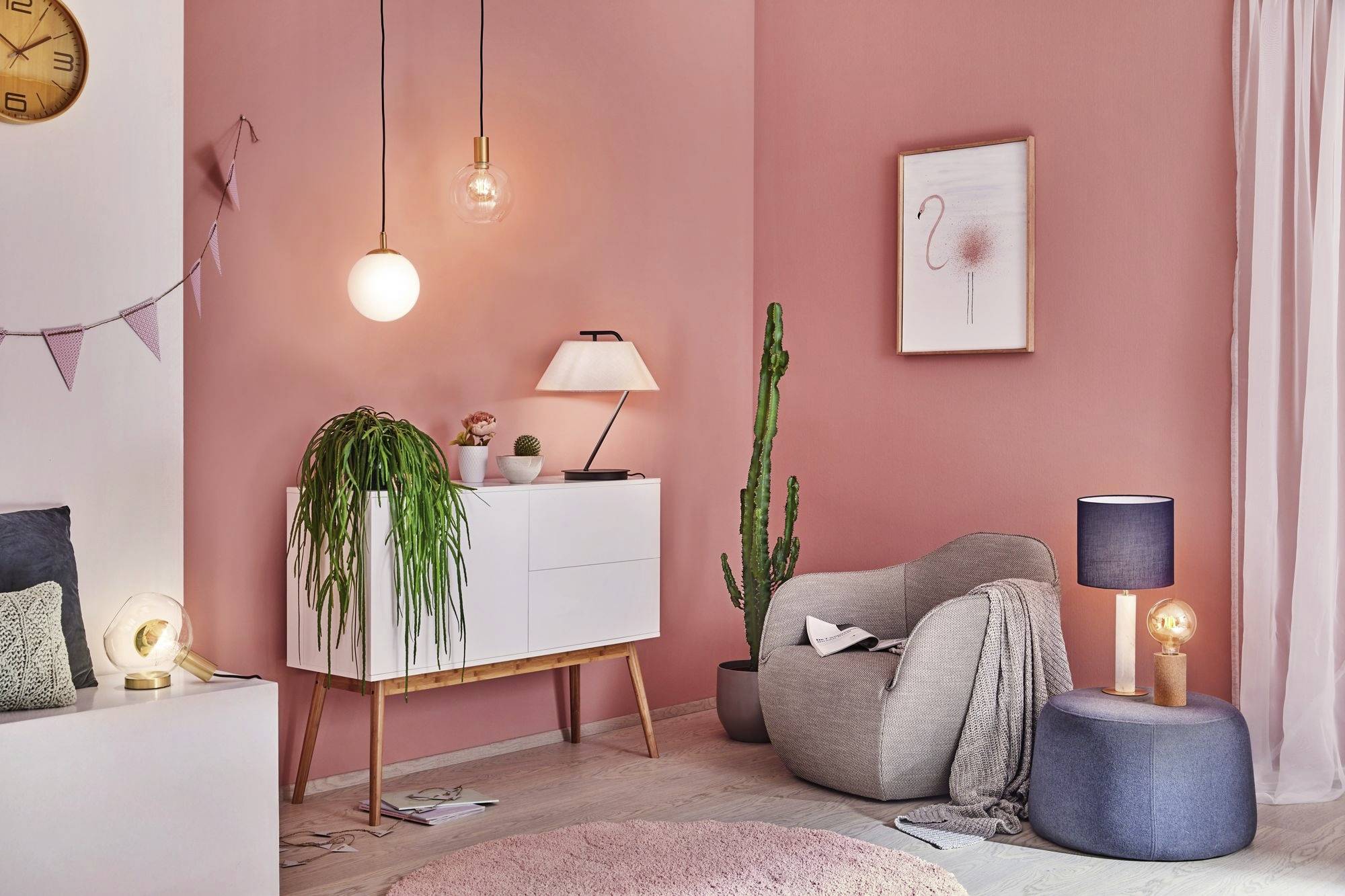 Gemütliches Wohnzimmer mit rosa Wänden, weißem Schrank, Leuchten, Pflanzen und bequemen Sesseln; stilvolle und warme Atmosphäre.