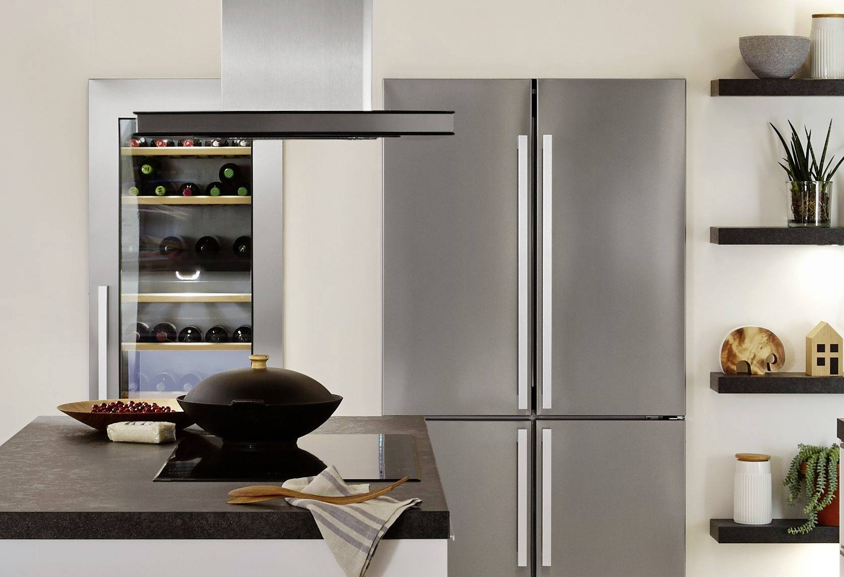 Moderne Küche mit Edelstahl-Kühlschrank, Weinkühler, Kochfeld und Dunstabzug. Dekorregale mit Pflanzen und Deko-Elementen an der Wand.