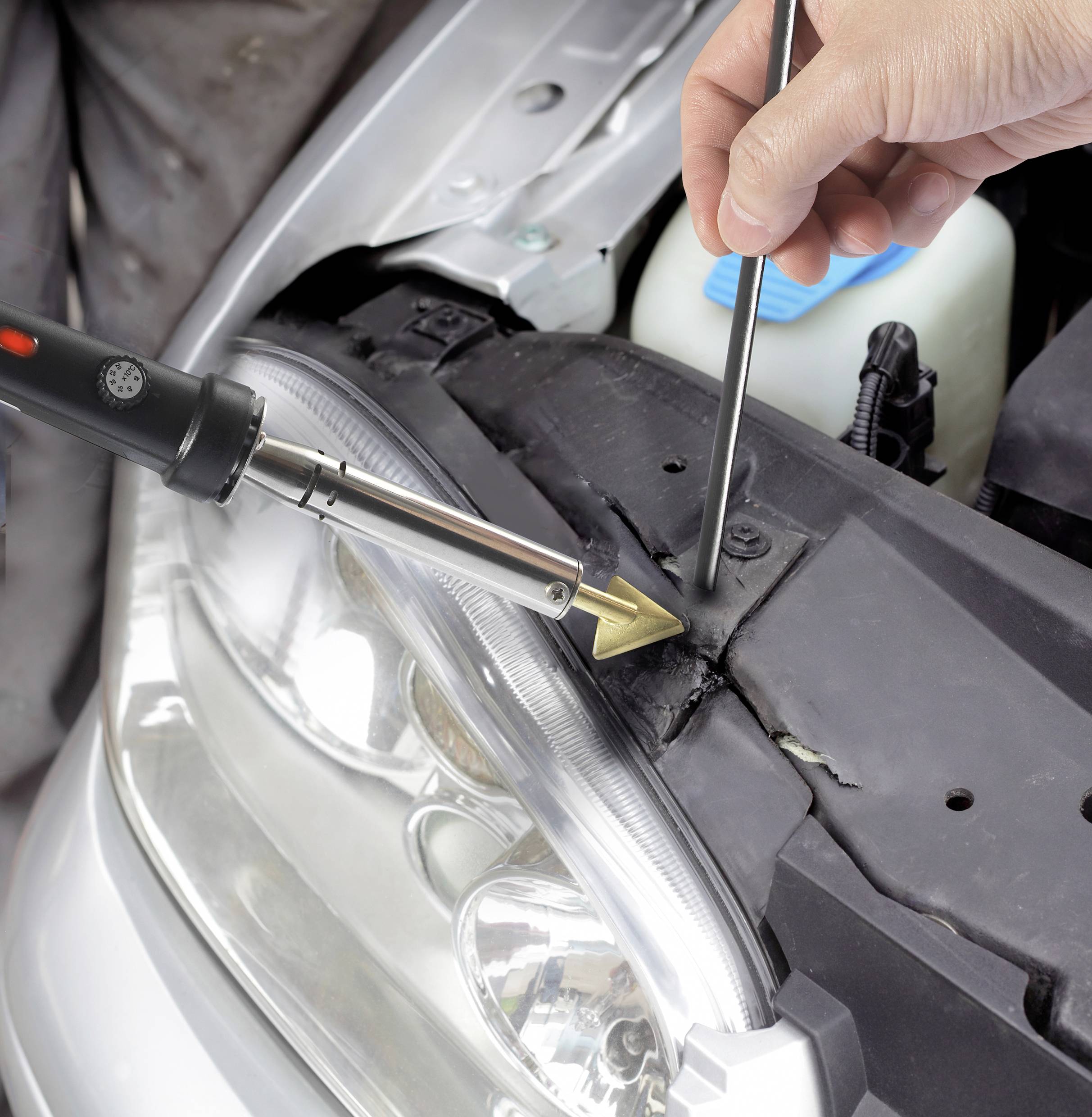 Jemand repariert den Kunststoff an einem Autoteil mit einem Lötkolben und einem Werkzeug, das Druck ausübt, um das Material zu formen.