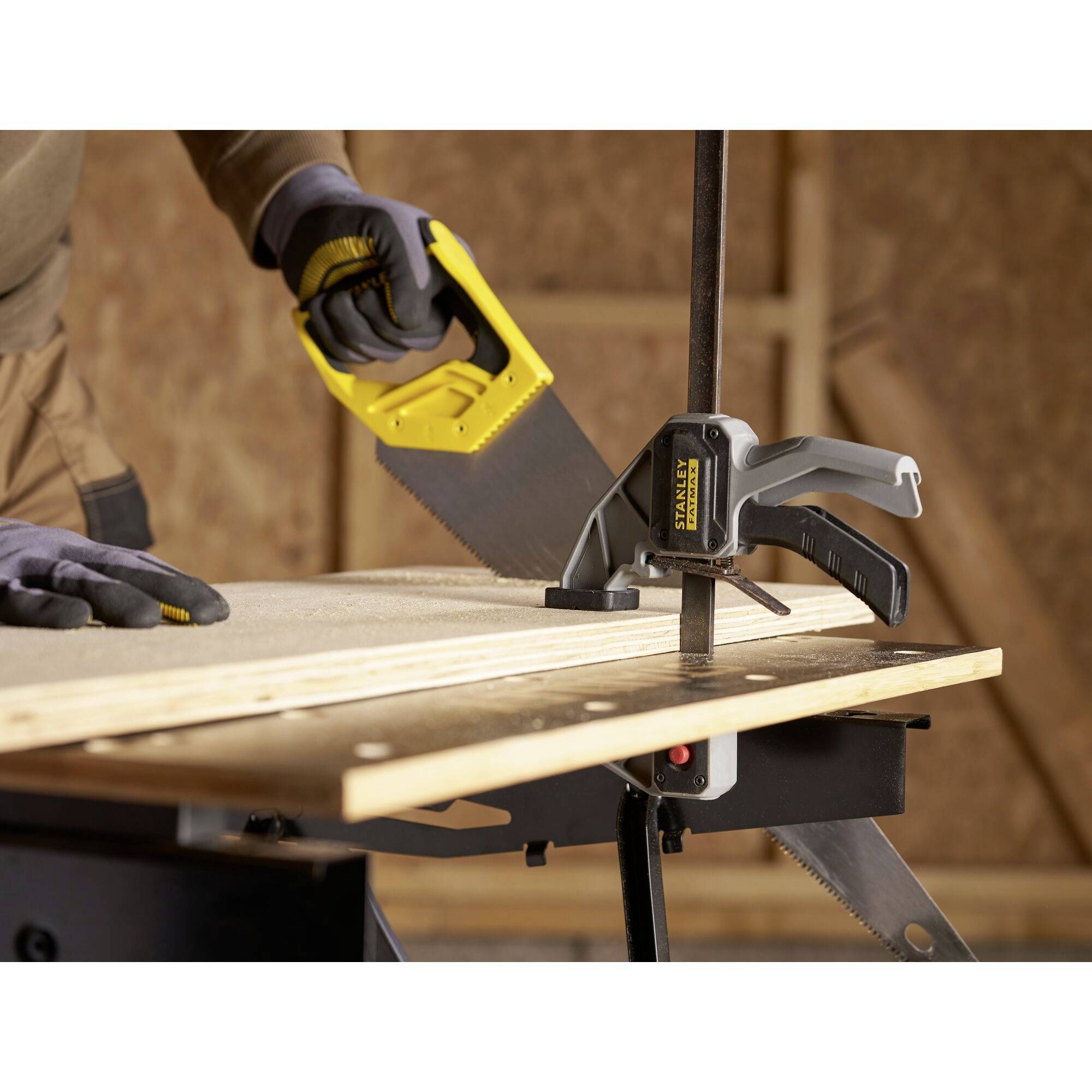 Eine Person sägt ein Holzbrett mit einer Handsäge, das mit einer Klemme auf einem Arbeitstisch fixiert ist.