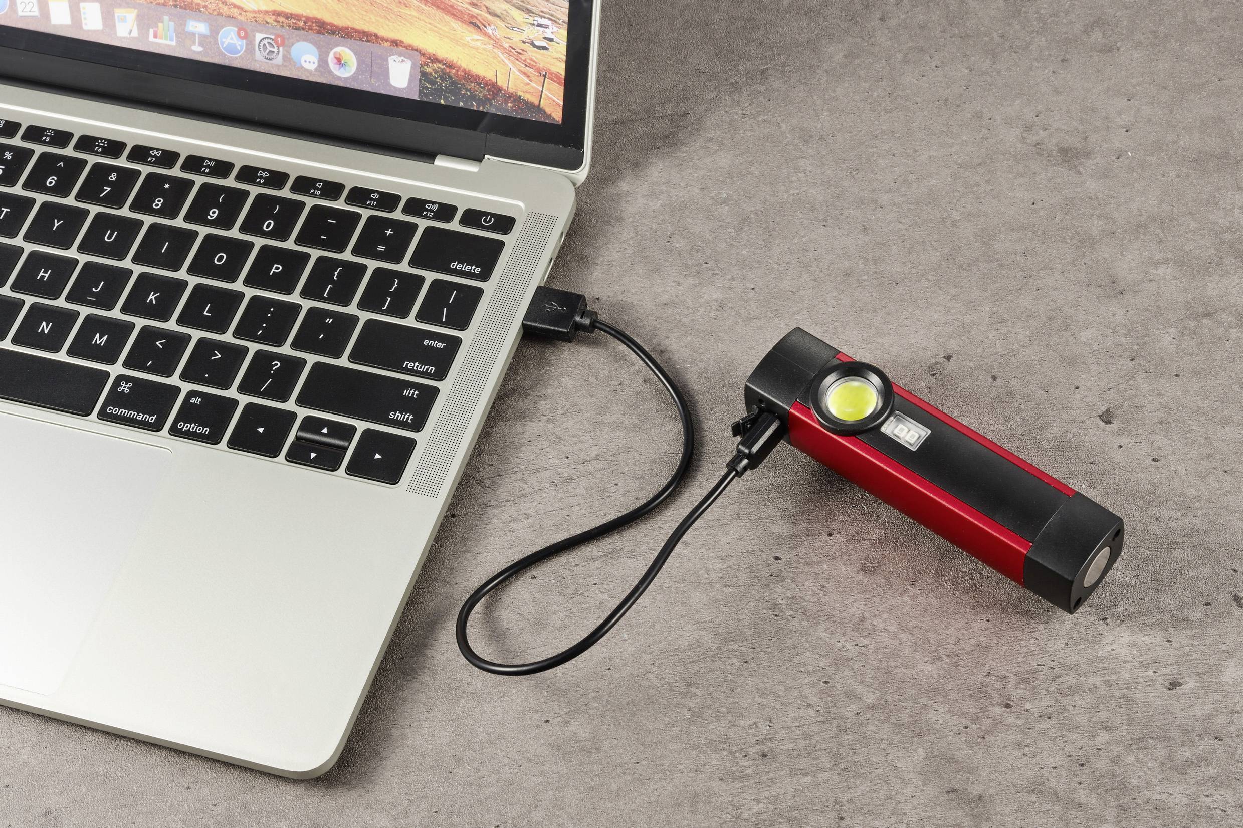 Eine rote Taschenlampe wird mit einem USB-Kabel an einen Laptop angeschlossen, der auf einem Tisch liegt.