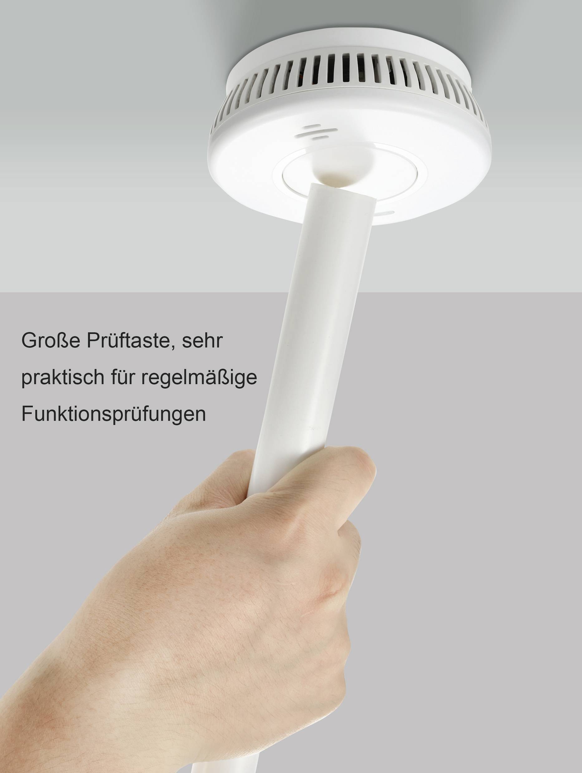 Eine Hand testet einen runden Rauchmelder an der Decke mit einer langen Stange. Text: 'Große Prüftaste, sehr praktisch für regelmäßige Funktionsprüfungen'.