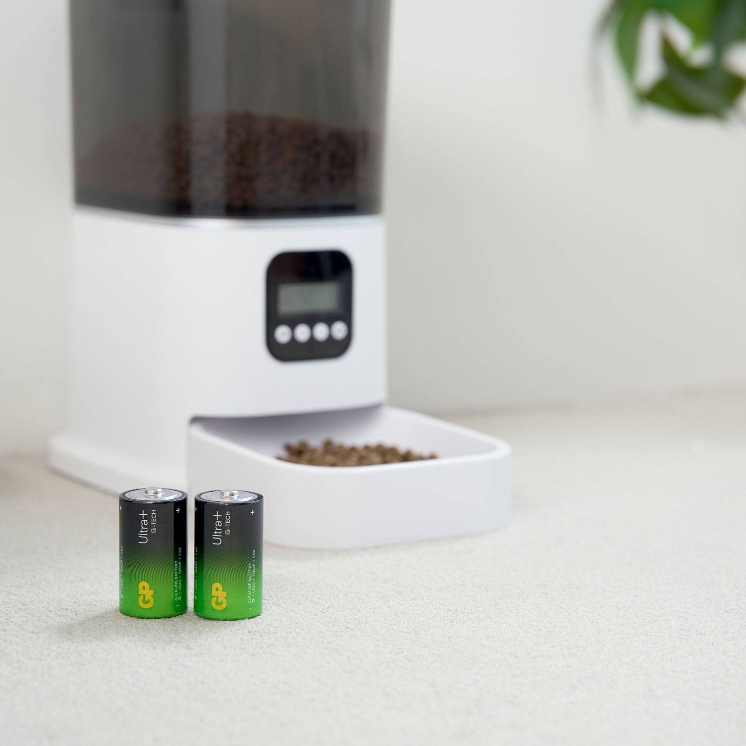 Ein Futterautomat gibt Trockenfutter in eine Schale ab. Im Vordergrund stehen zwei Batterien der Marke GP.