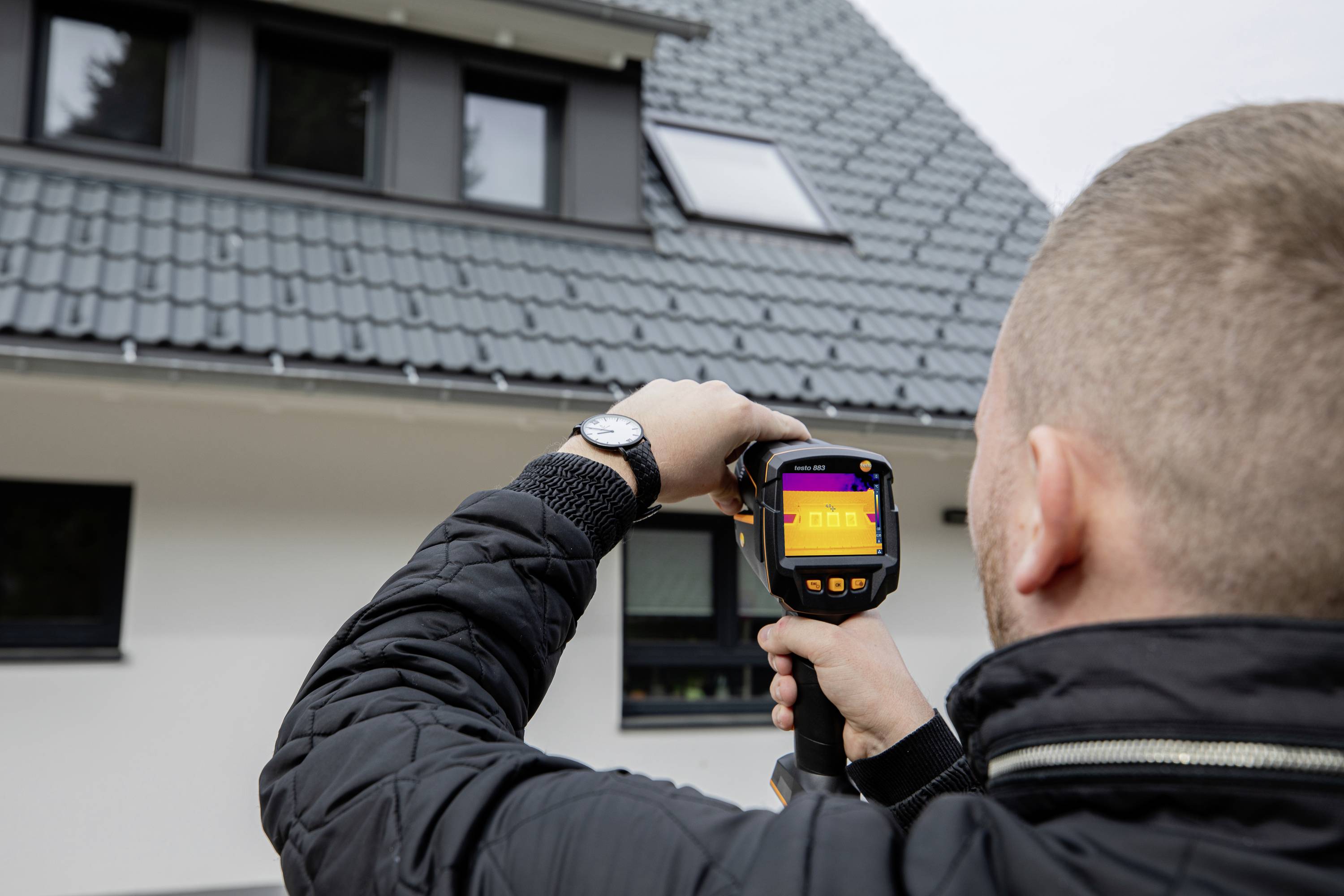 Eine Person hält eine Wärmebildkamera vor einem Haus und überprüft die Isolierung des Daches.