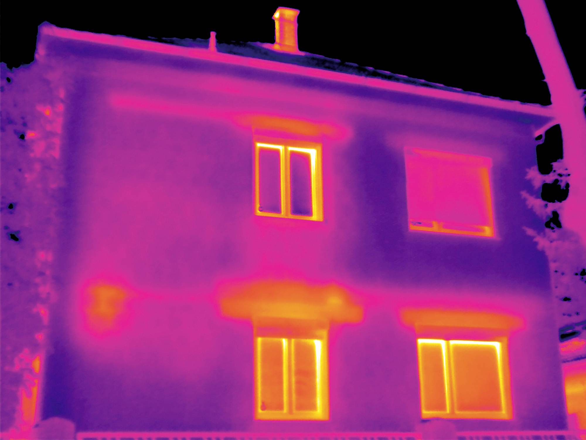 Eine Wärmebildaufnahme eines zweistöckigen Hauses. Helle Bereiche zeigen Wärmeverlust an Fenstern und Wänden.
