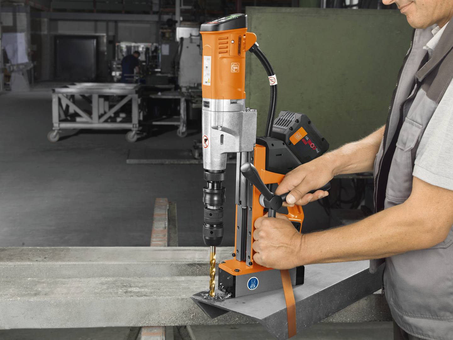 Eine Person bedient eine magnetische Bohrmaschine in einer Werkstatt, um präzise Löcher in einen Metallträger zu bohren.