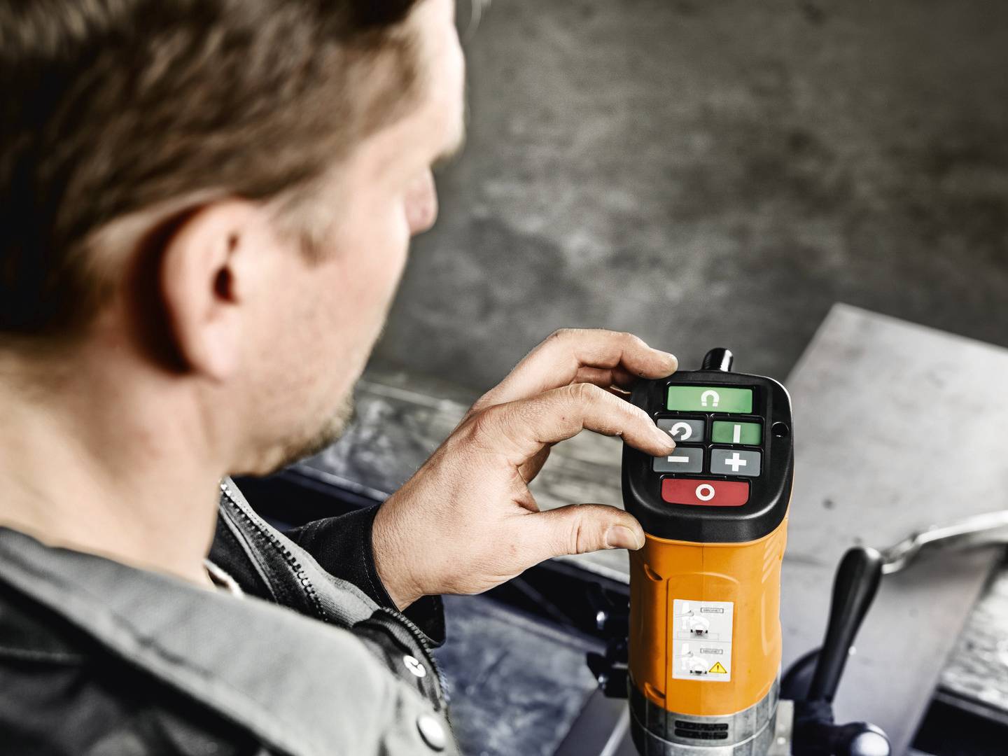 Ein Mann bedient ein elektronisches Steuergerät mit einem Display und Tasten in Farbcodierung, das auf einem industriellen Gerät montiert ist.