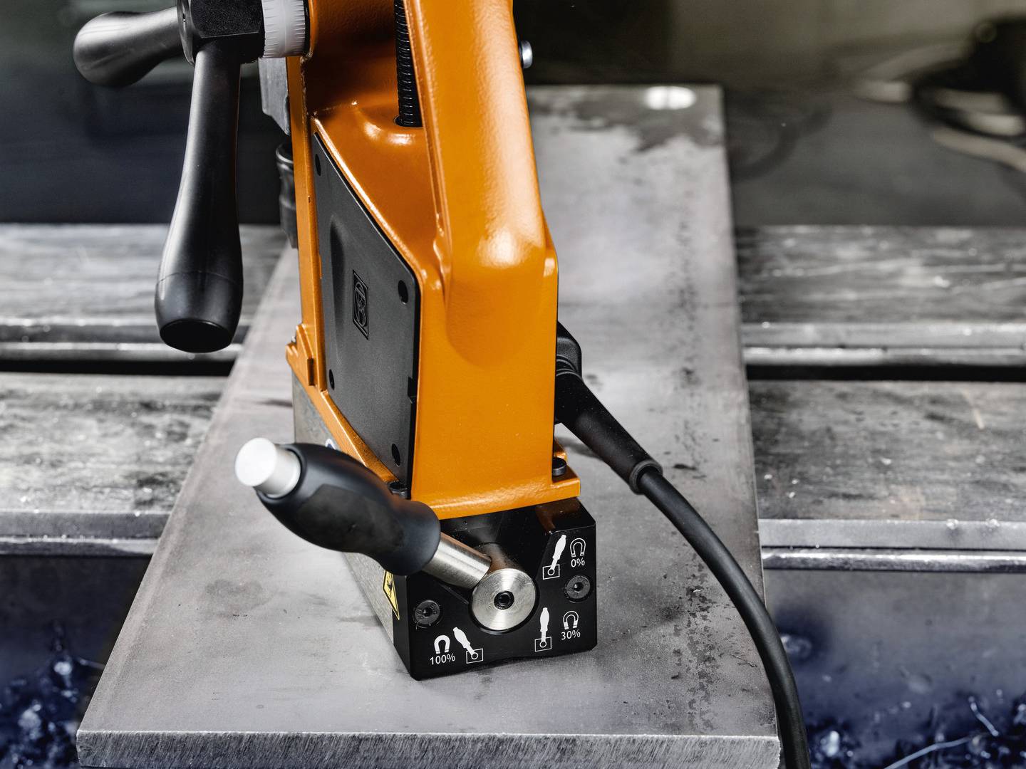 Ein orangefarbenes magnetisches Bohrwerkzeug ist auf einer Metallplatte positioniert, bereit zur Verwendung.