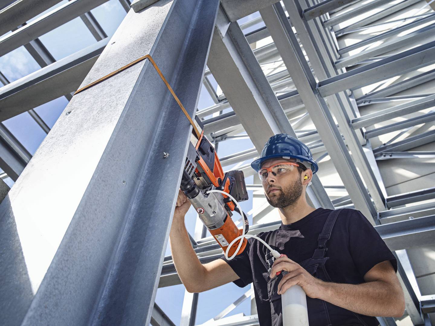 Ein Arbeiter mit Helm und Schutzbrille bearbeitet einen Metallträger in einem Gebäude aus Stahlträgern, verwendet eine elektrische Säge.