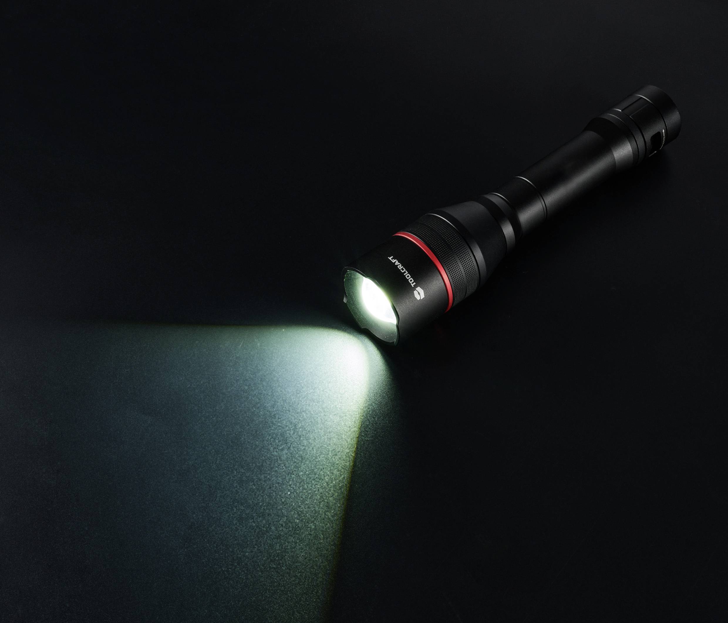 Schwarze Taschenlampe strahlt Lichtstrahl auf dunklem Hintergrund aus. Hauptmotiv ist die Funktionsweise und Wirkung der Taschenlampe.
