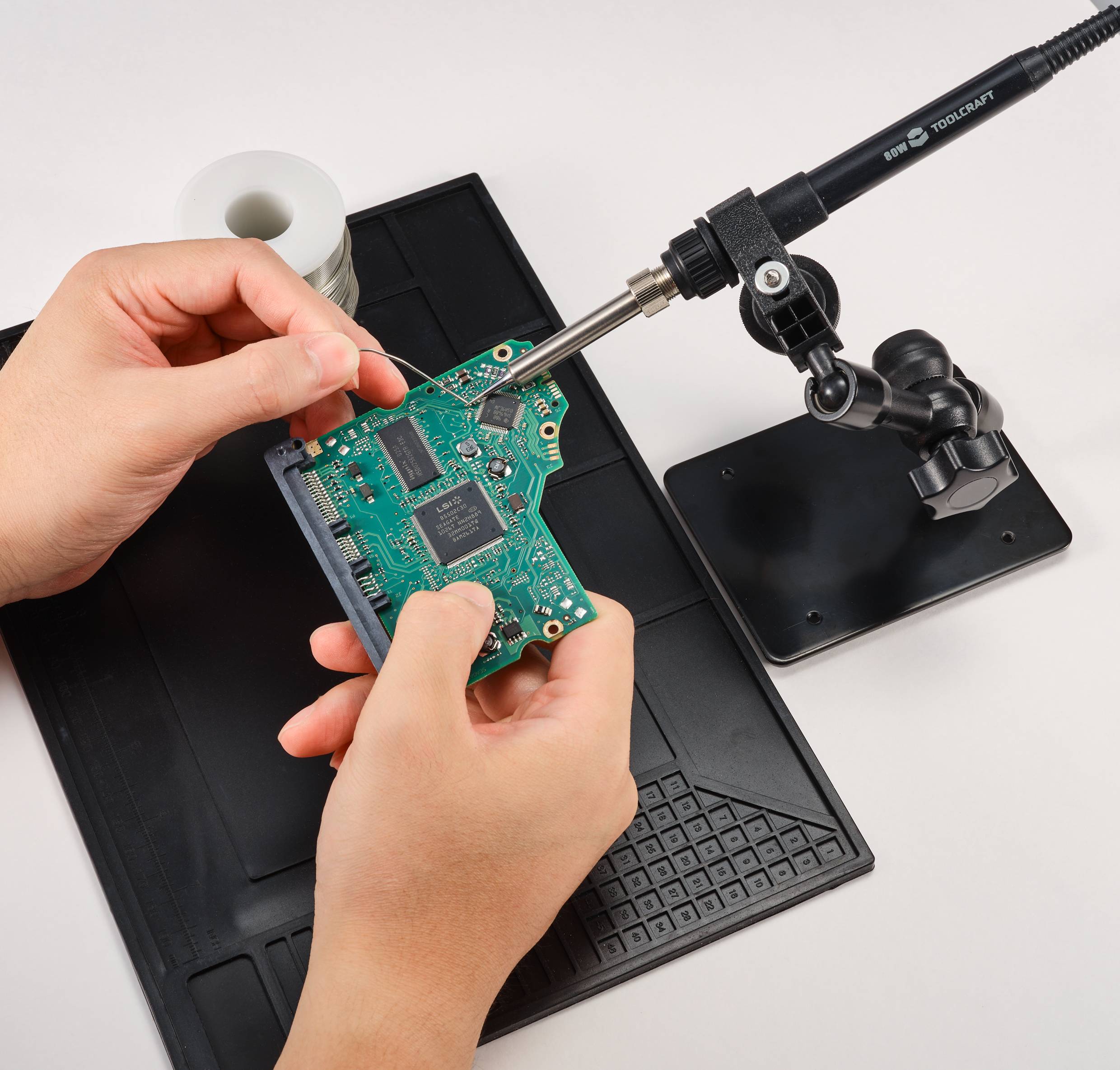 Person lötet eine grüne Leiterplatte mit einem Lötkolben. Die Szene zeigt präzises Arbeiten bei der Elektronikreparatur.