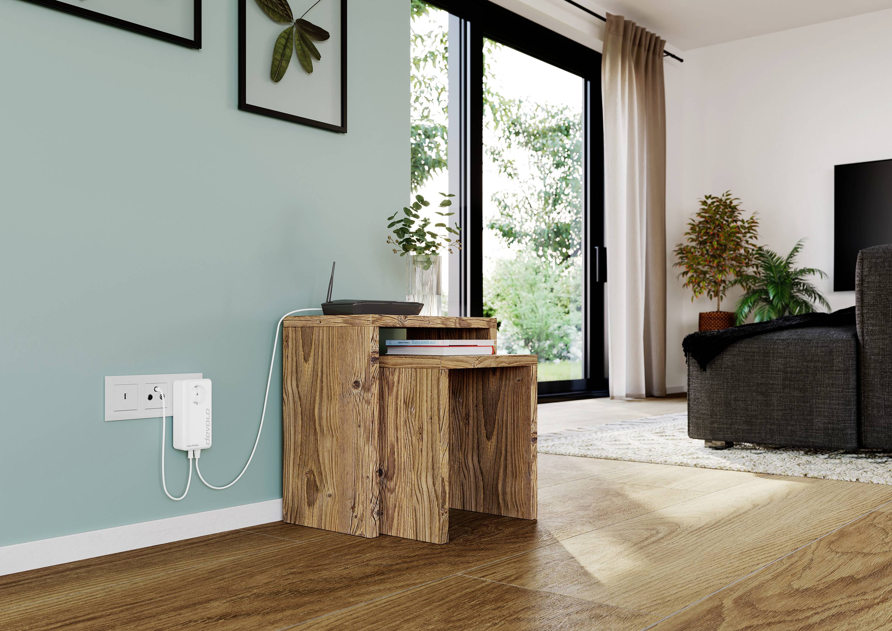 Holztisch mit Router, an Steckdose angeschlossen. Links grüne Wand mit Bildern, rechts Glastür mit Blick auf Garten. Wohnzimmerumgebung.