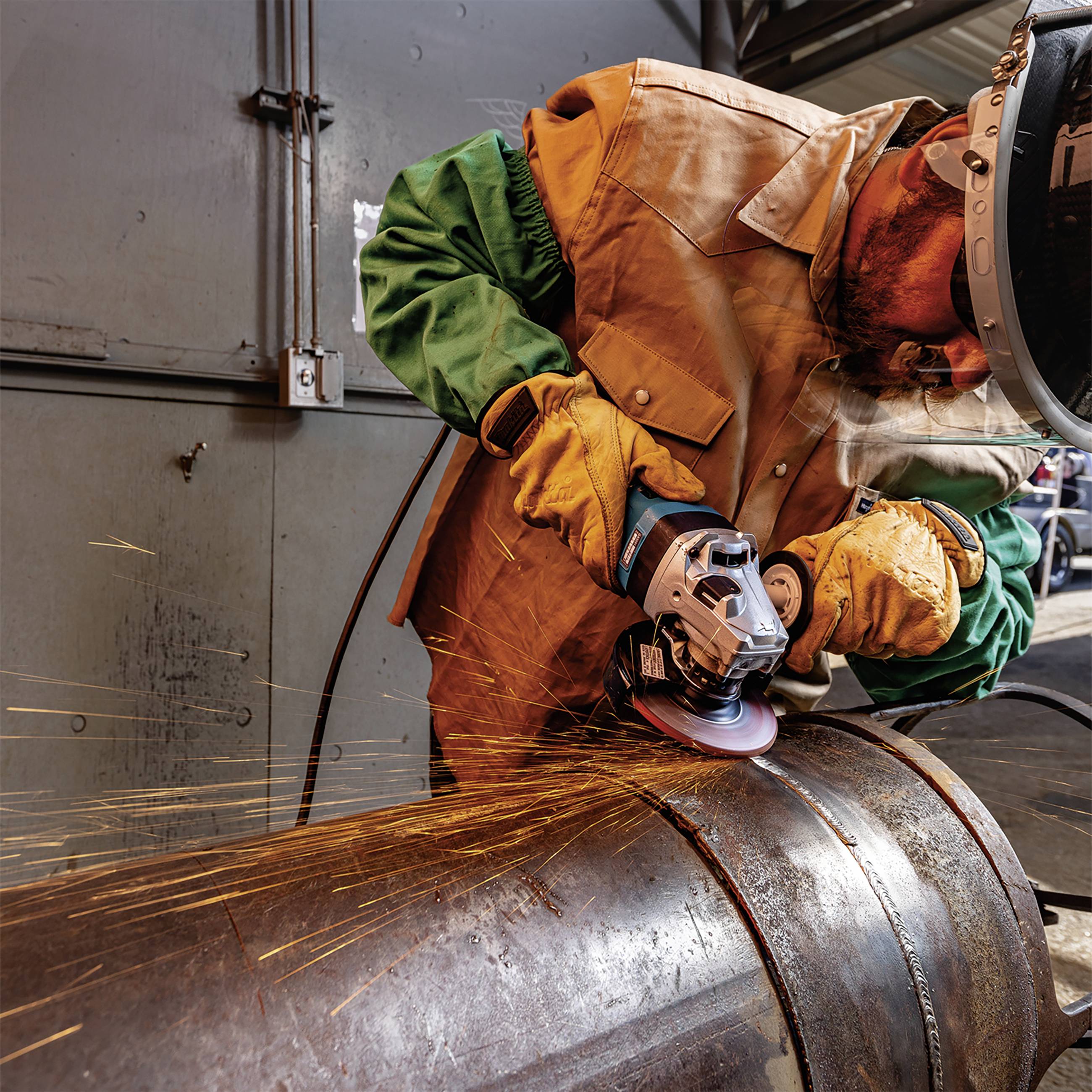 Ein Arbeiter schneidet mit einem Winkelschleifer Metall. Funken fliegen. Der Arbeiter trägt Schutzkleidung und -brille.