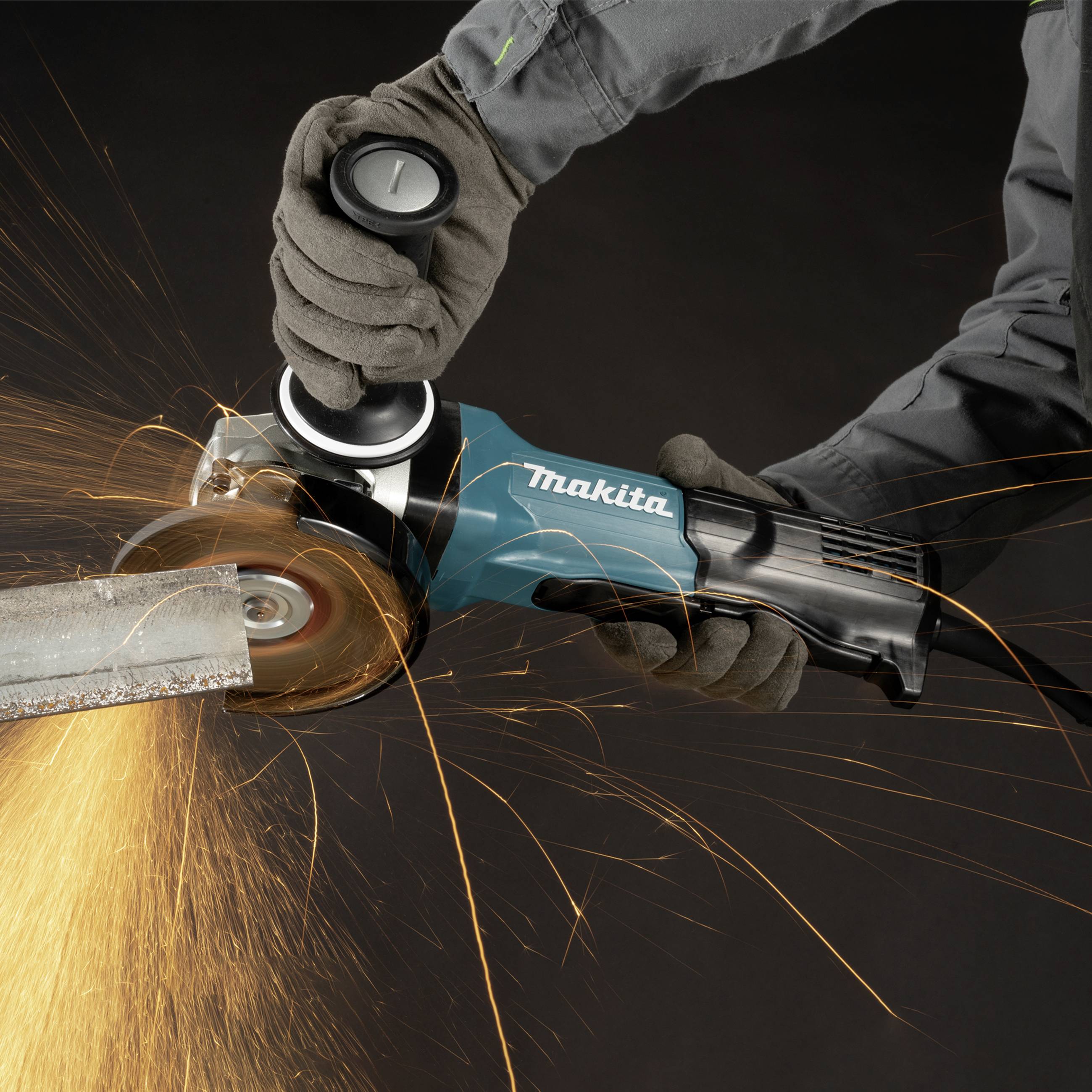Ein Handwerker mittlerer Hand schneidet mit einem blauen Winkelschleifer ein Metallrohr, Funken fliegen.