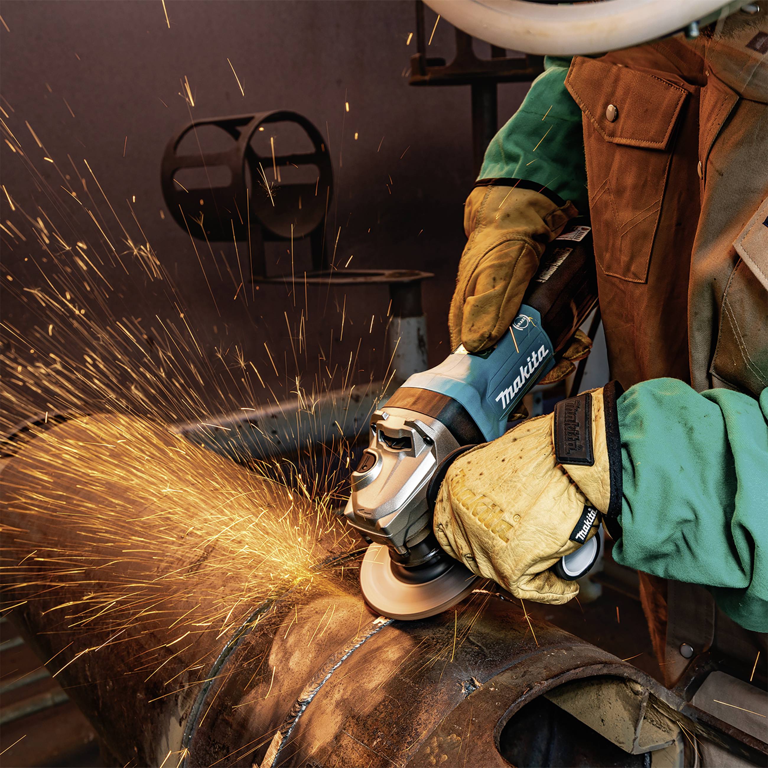 Eine Person schleift mit einem Winkelschleifer Metall, Funken sprühen. Schutzhandschuhe und grüne Jacke werden getragen.