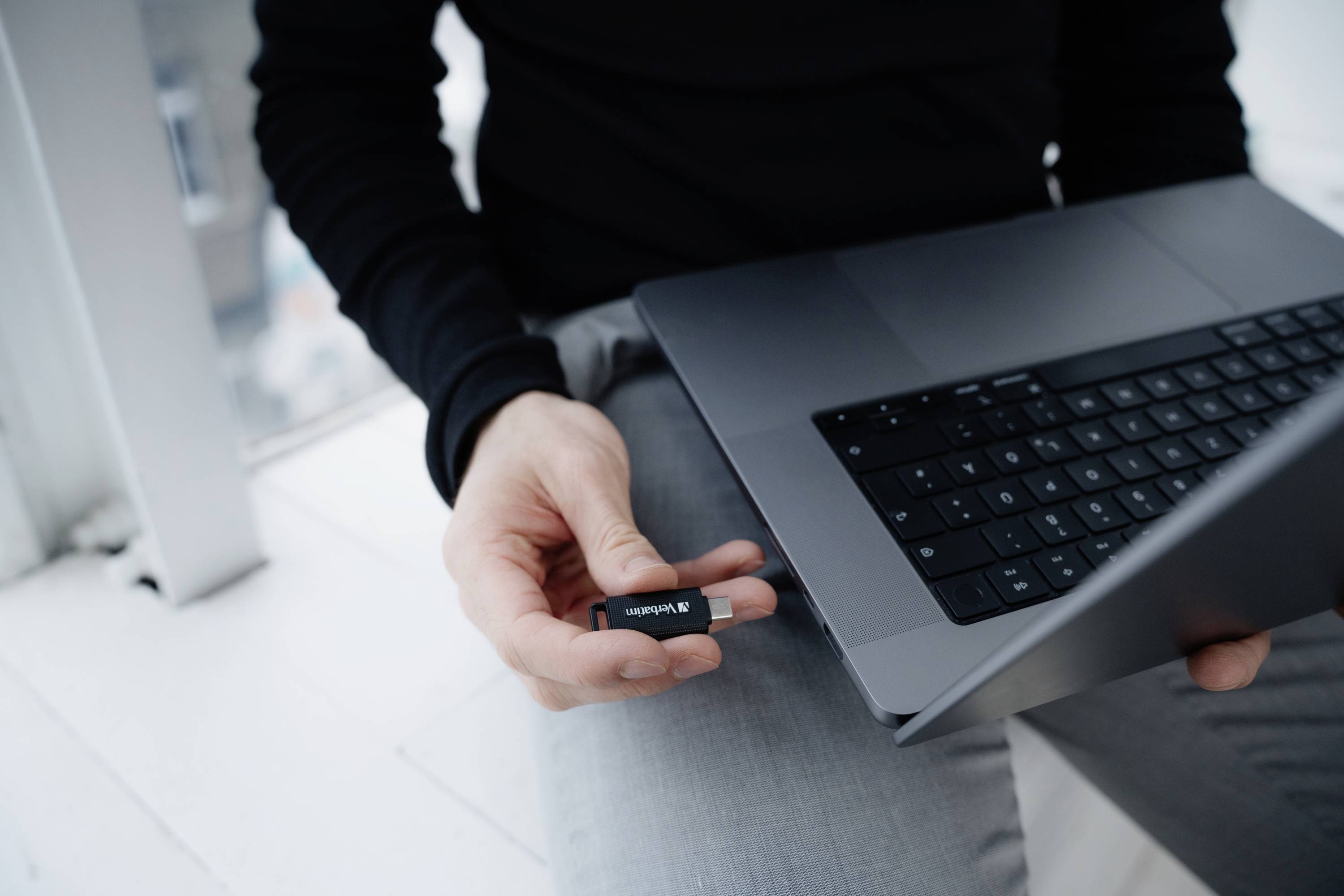 Eine Person hält einen USB-Stick in der Hand und steht kurz davor, ihn in einen Laptop einzustecken.