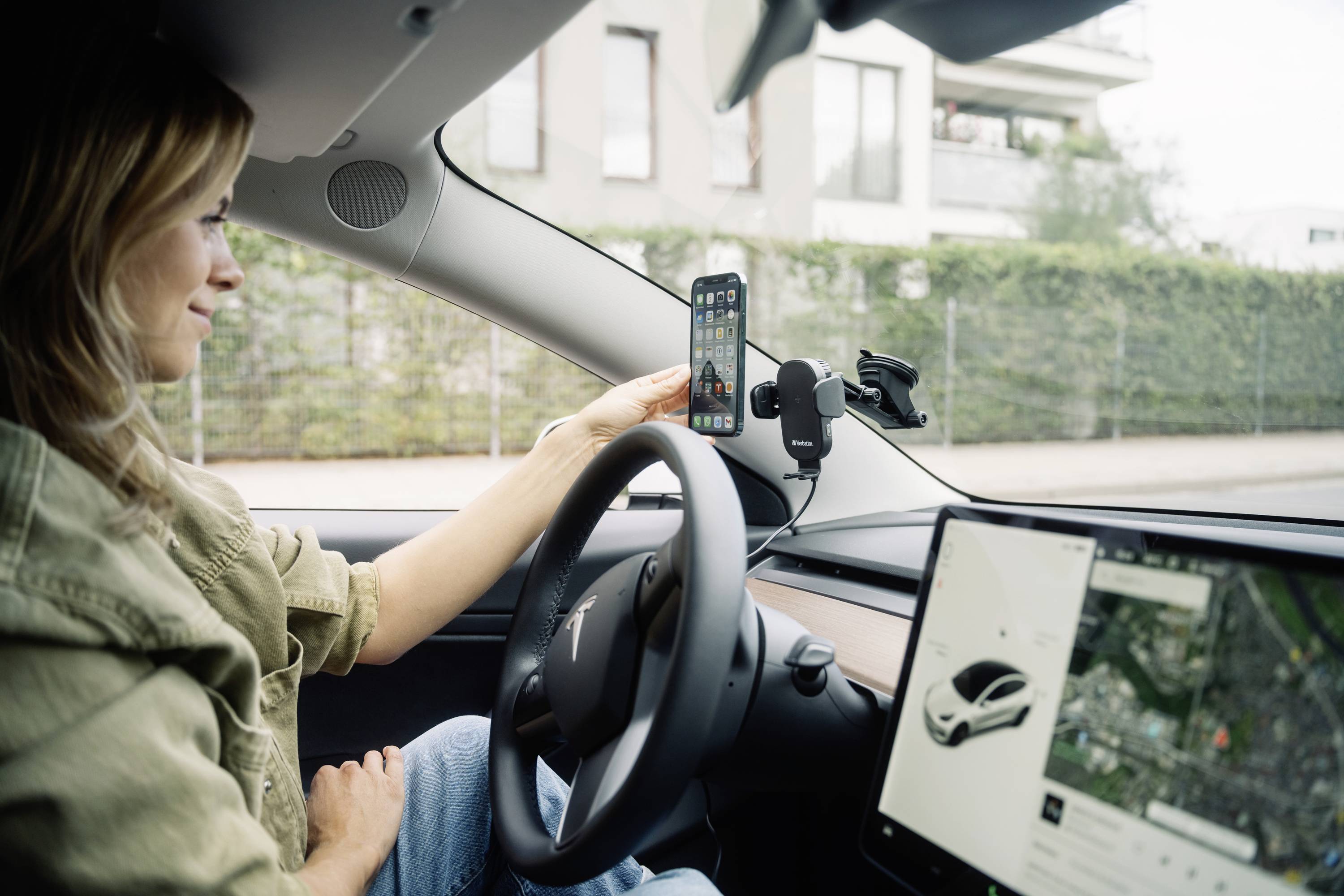 Eine Person sitzt in einem Auto und befestigt ein Smartphone an der Halterung am Armaturenbrett. Das Auto zeigt ein Navigationssystem.