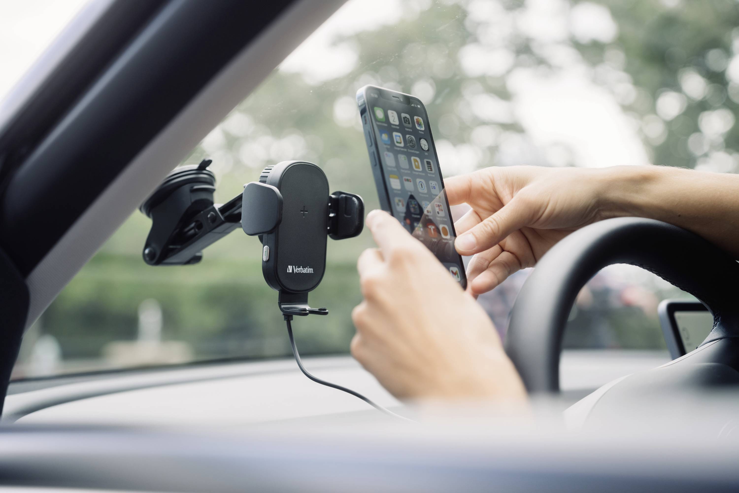 Eine Person befestigt ein Smartphone an einer Handyhalterung im Auto. Die Halterung ist an der Windschutzscheibe angebracht.