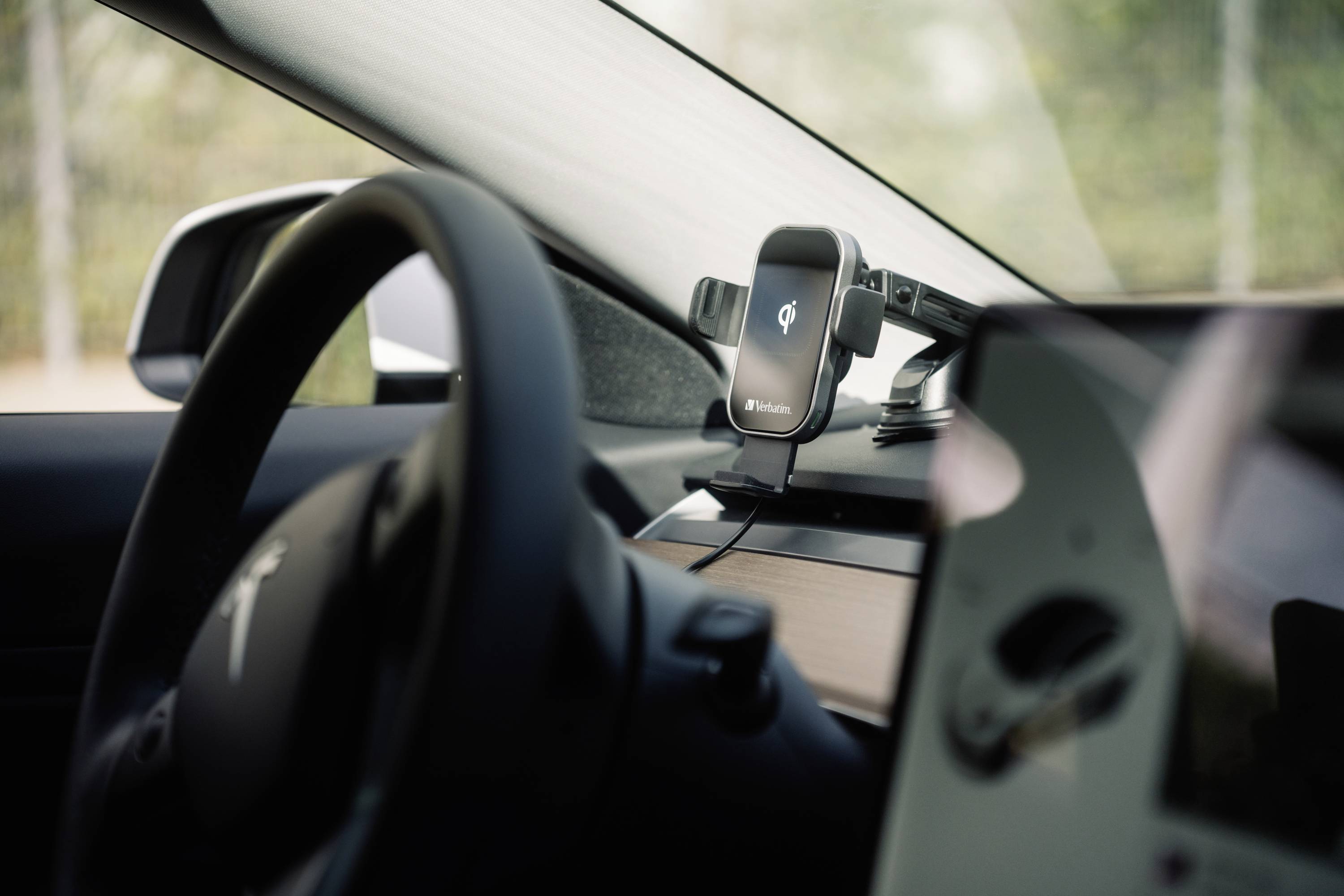 Lenkrad und Handyhalterung in einem modernen Auto mit zentralem Bildschirm, unklarer Bildschirminhalt.
