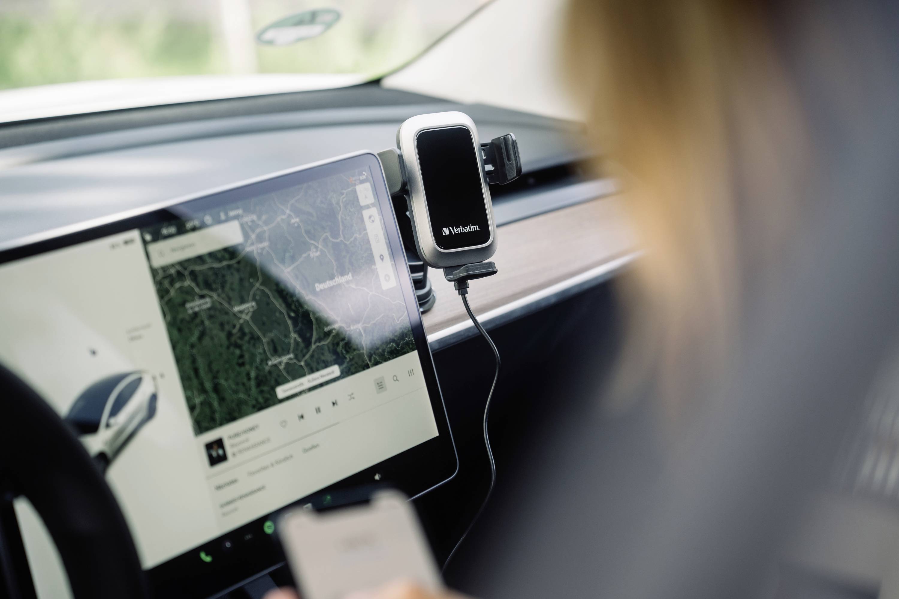 Eine Person im Auto bedient ein Smartphone. Ein GPS-Navigationssystem auf dem Display zeigt eine Kartenansicht an.