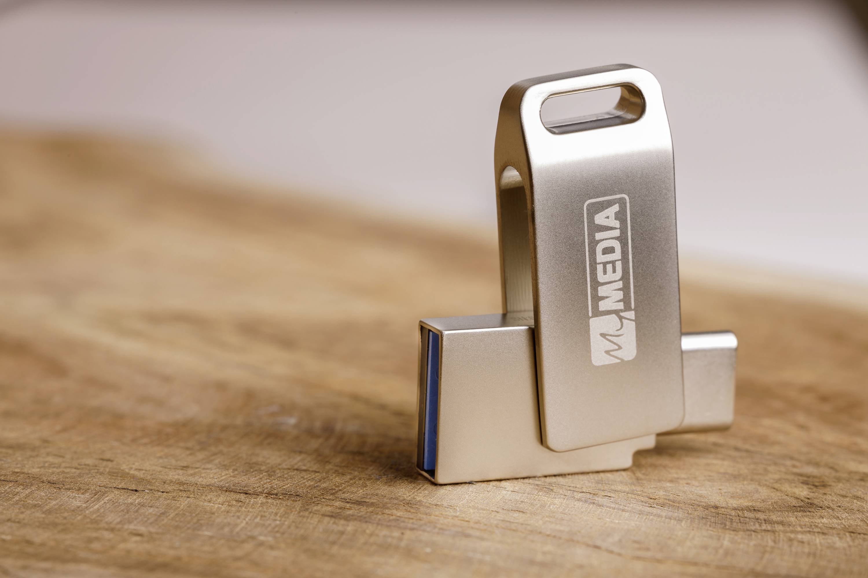 Ein USB-Stick mit dem Logo 'MJ MEDIA' liegt auf einer Holzoberfläche. Der Stick ist aus Metall und teilweise geöffnet.