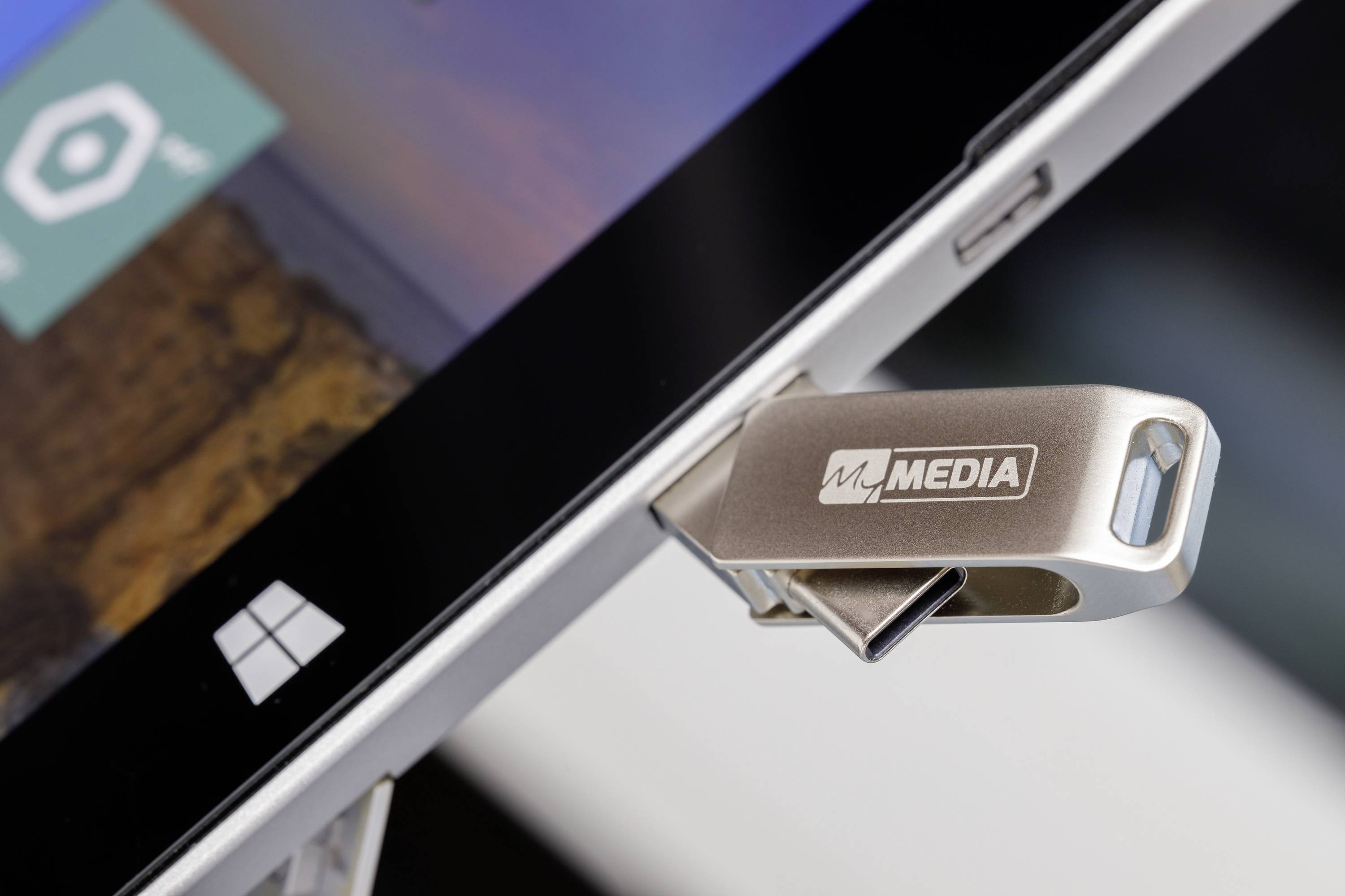 Ein USB-Stick mit der Aufschrift 'MEDIA', eingesteckt in einen Laptop. Bildschirm zeigt Teile der Benutzeroberfläche.
