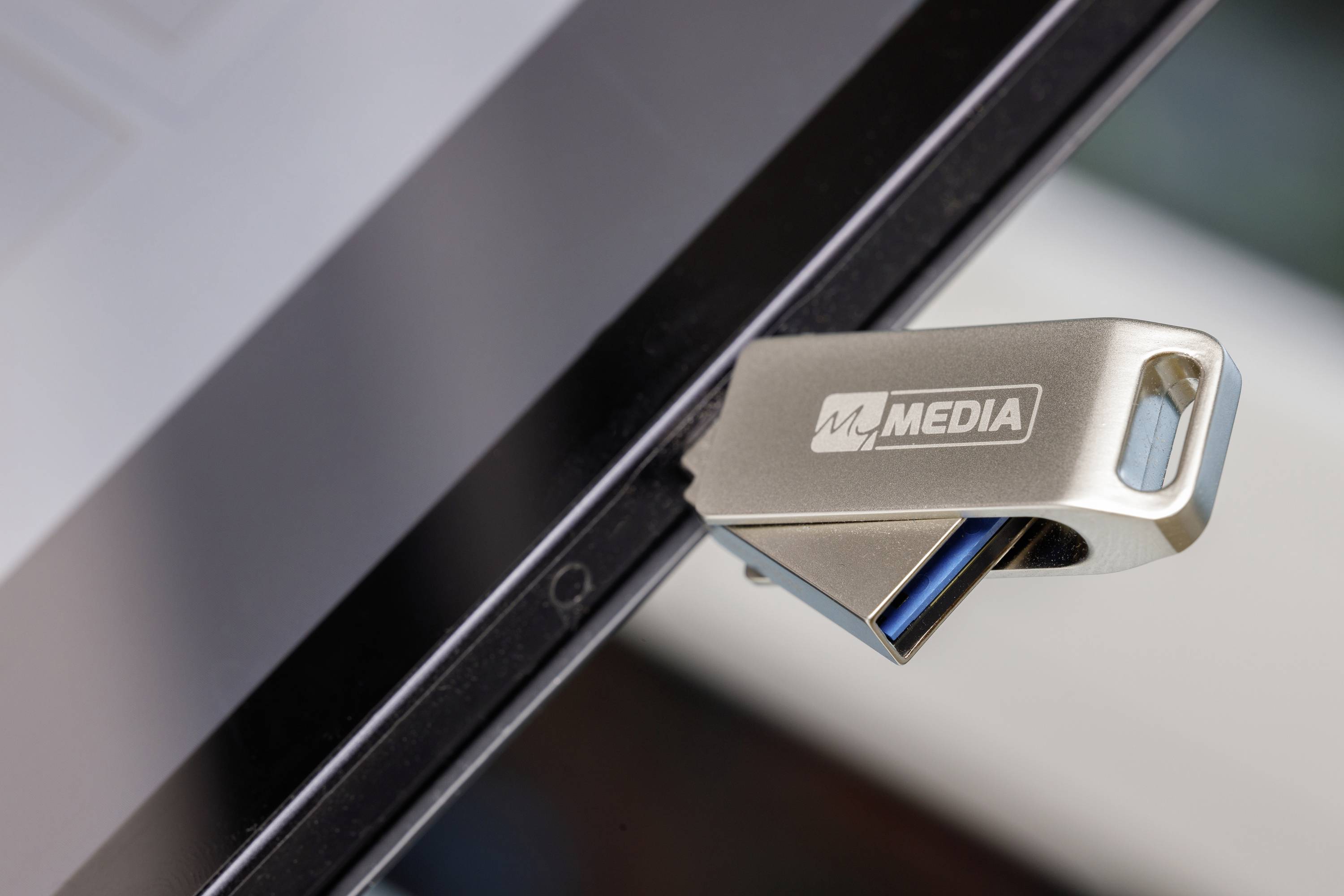 Ein silberner USB-Stick mit der Aufschrift 'MEDIA' ist in einen Laptop eingesteckt. Der Laptop ist teilweise sichtbar.