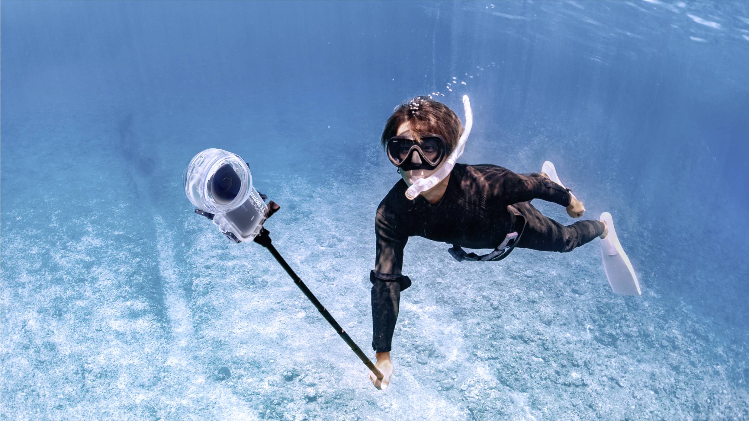 Eine Person schnorchelt unter Wasser und hält eine Kamera an einem langen Stab. Die Umgebung ist klar und blaues Wasser umgibt sie.