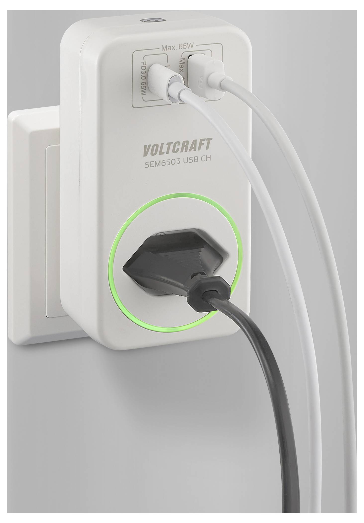 Ein weißes Voltcraft-Strommessgerät, das in eine Steckdose gesteckt ist, zeigt zwei USB-Kabel und ein Stromkabel an, die angeschlossen sind, mit einem leuchtenden grünen Ring.