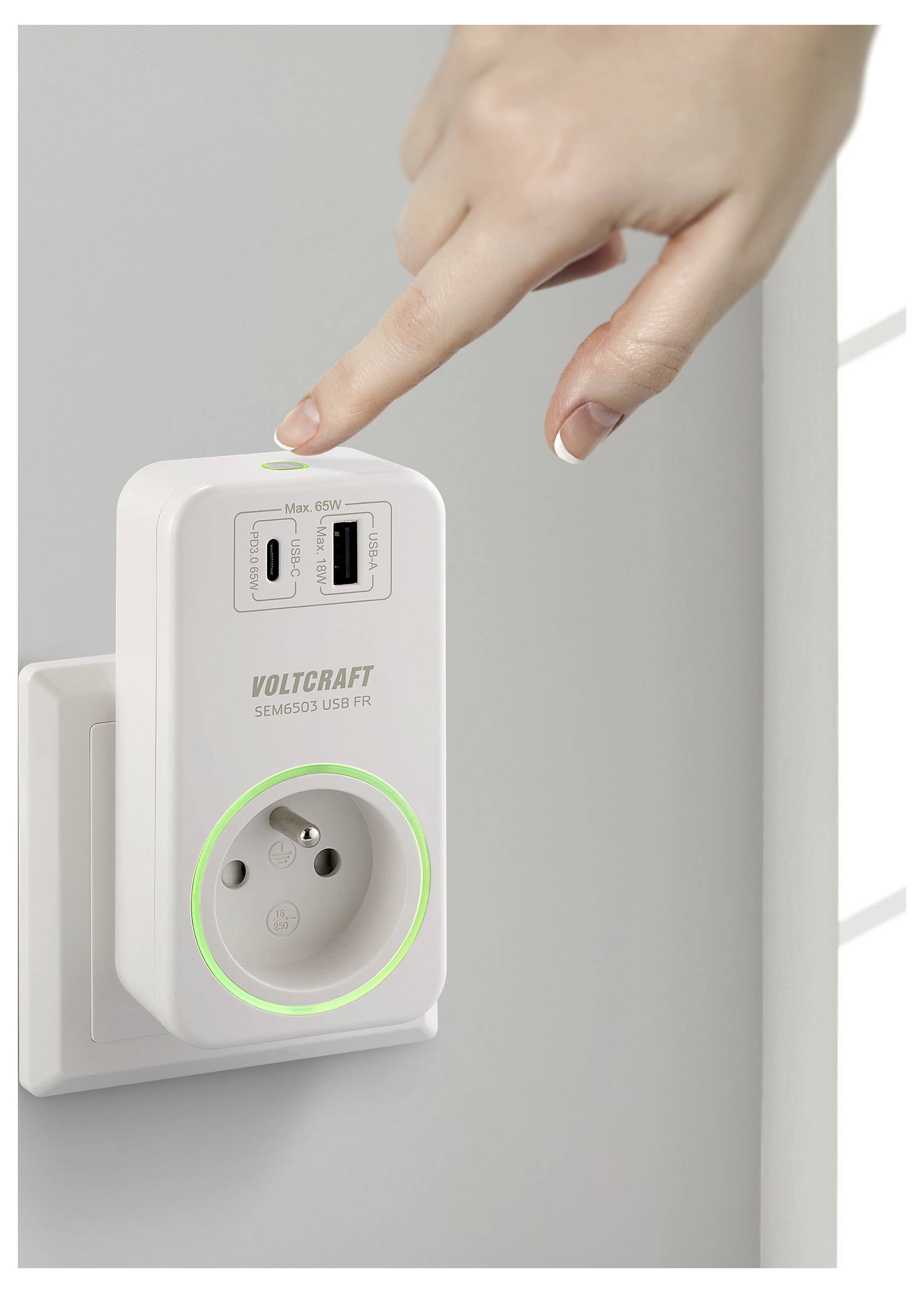 Eine Hand greift, um auf einen Knopf an einer weißen Steckdose mit USB-Anschlüssen zu drücken. Ein grüner Lichtkranz umgibt die Steckdose und zeigt an, dass sie eingeschaltet ist.