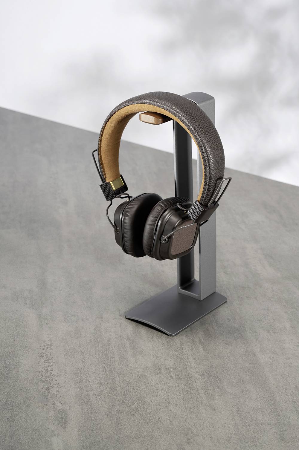 Schwarze Kopfhörer mit Bügel auf einem grauen Ständer, auf einem Tisch stehend. Hintergrund unscharf, Fokus auf Hörer und Ständer.