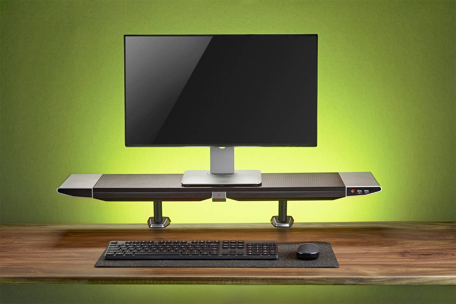 Ein Computerbildschirm auf einem erhöhten Schreibtischregal, umgeben von grünem Licht, mit Tastatur und Maus auf dem Holztisch.