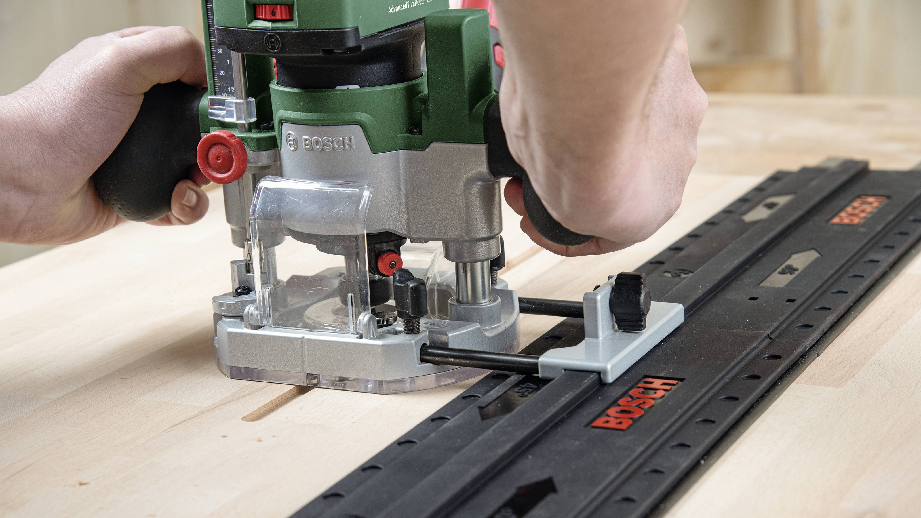 Eine Fräse von Bosch wird auf einer Führungsschiene zum Fräsen eines Holzteils verwendet. Hände halten die Fräse für präzises Arbeiten.