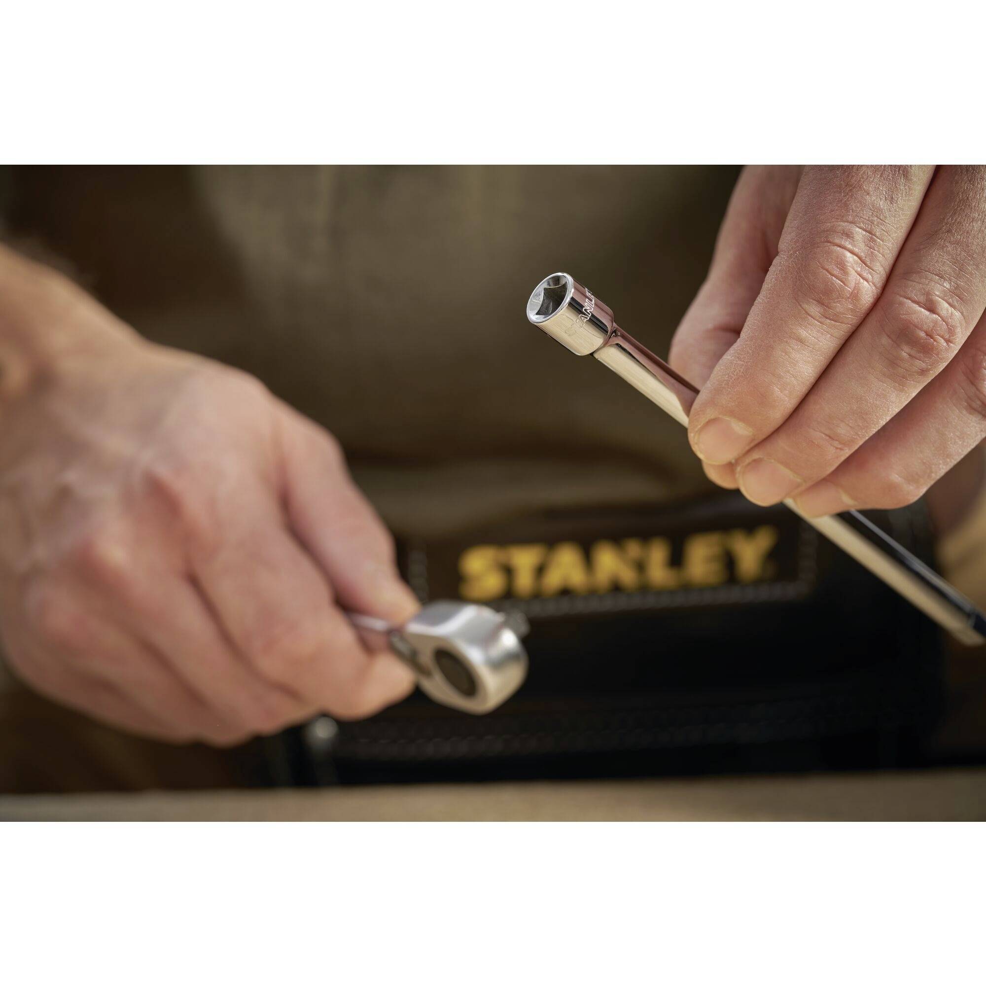 Eine Person hält eine Ratsche und einen Steckschlüssel mit einer Schlüsselfläche. Fokus auf Werkzeugbenutzung, Stanley-Schriftzug.