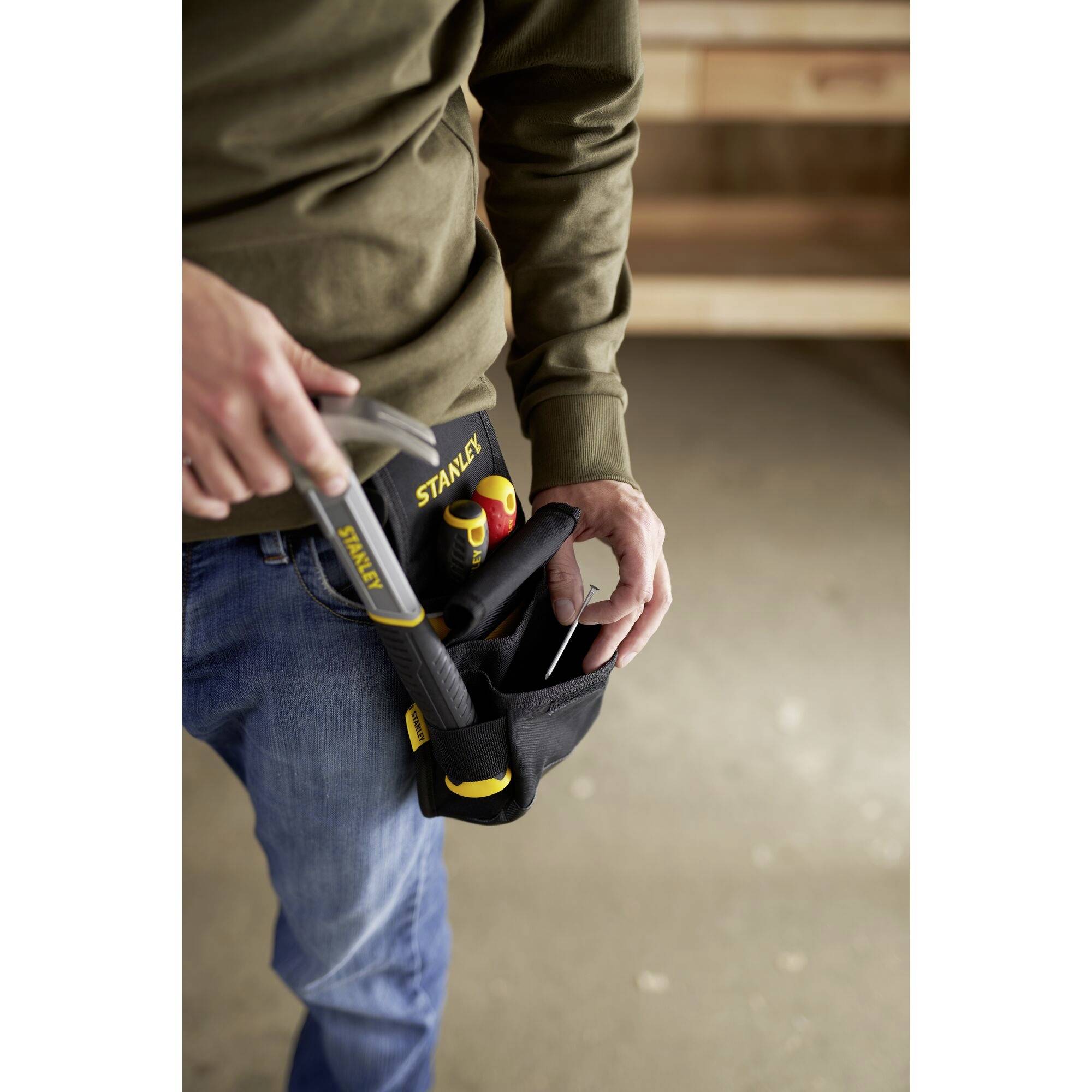 Ein Handwerker trägt eine schwarze Werkzeugtasche mit Hammer und anderen Werkzeugen, die gerade herausgenommen werden.