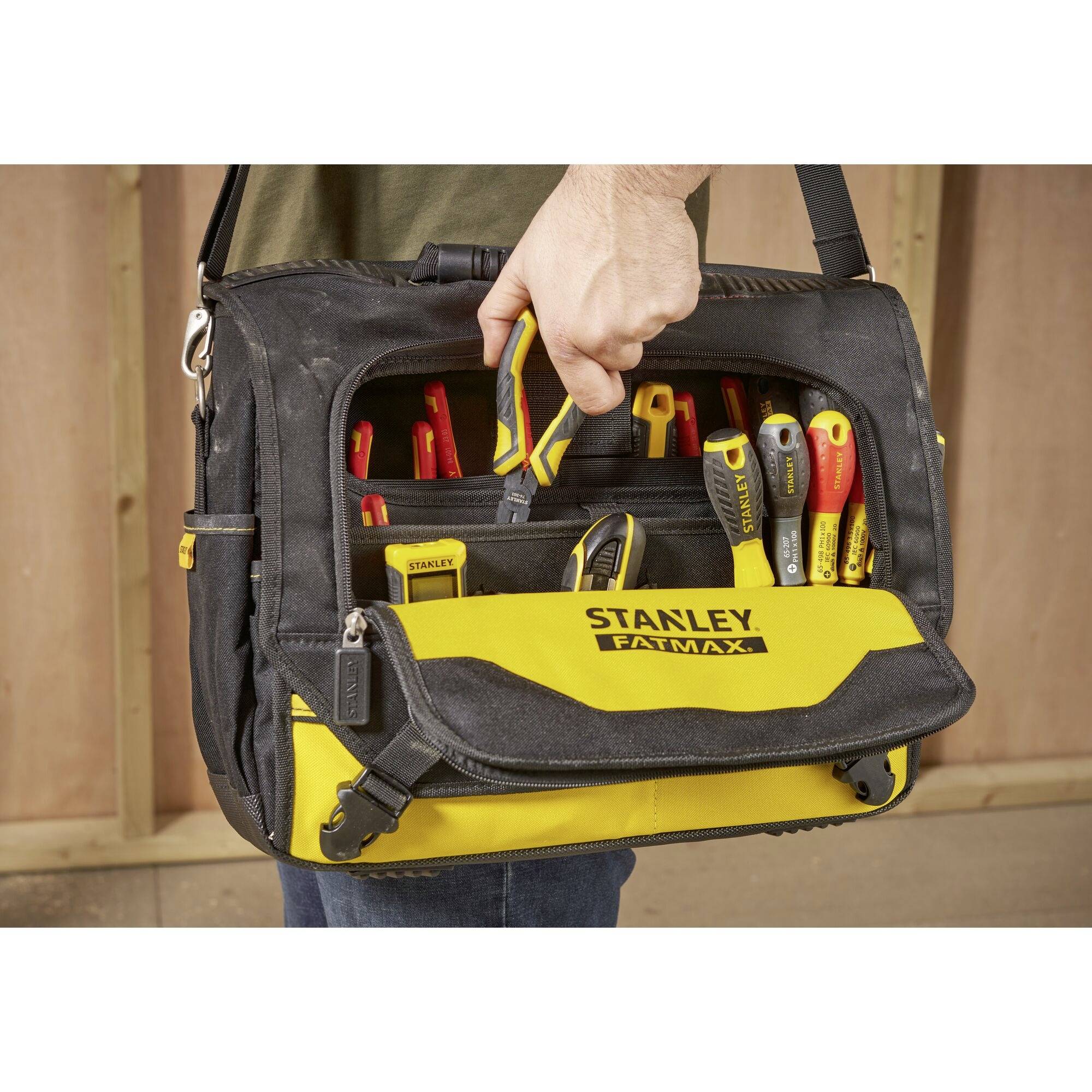 Eine Person hält eine schwarze und gelbe Werkzeugtasche mit verschiedenen Werkzeugen darin, darunter Schraubendreher und Zangen.
