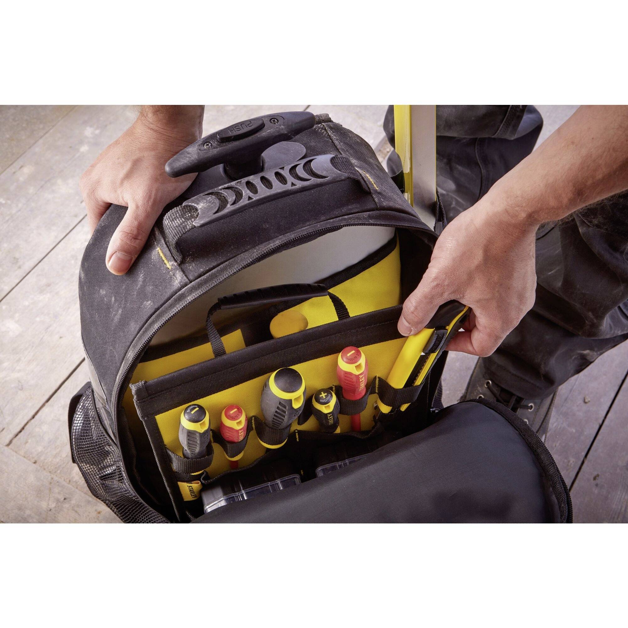 Werkzeugtasche mit verschiedenen Handwerkzeugen, einschließlich Schraubendrehern und Zangen, wird von zwei Händen geöffnet.